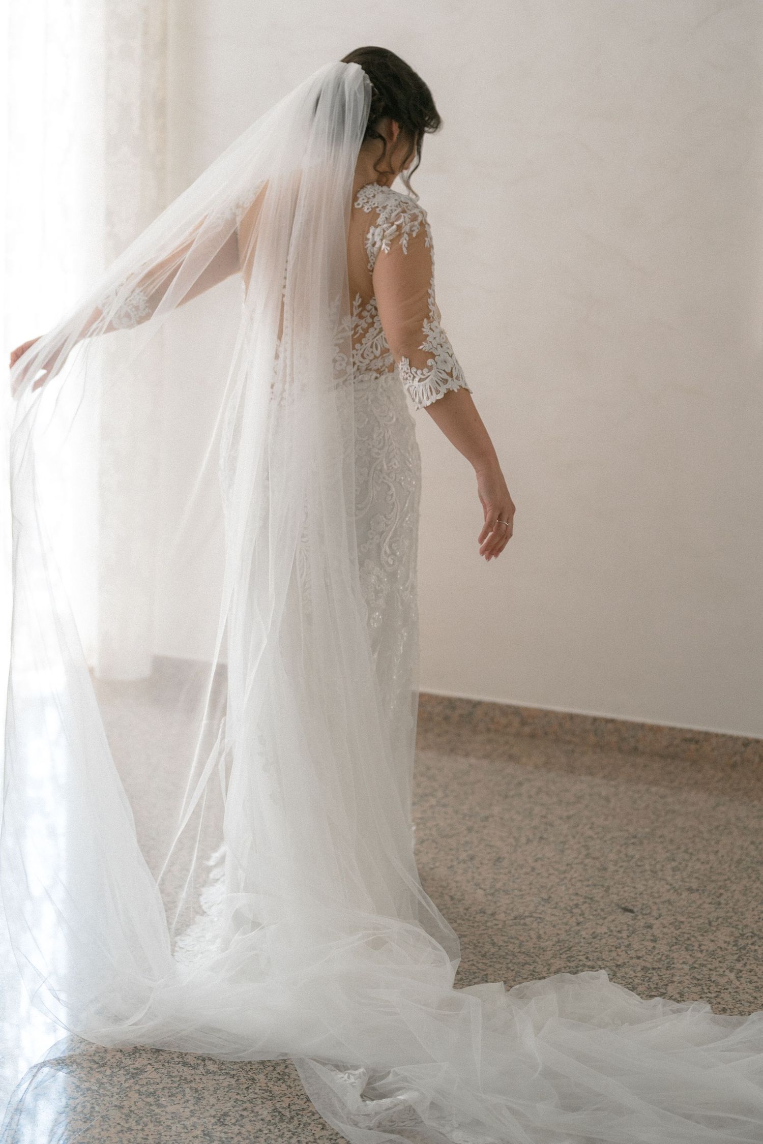 Flowing white wedding dress with lace details and long veil captured in motion.