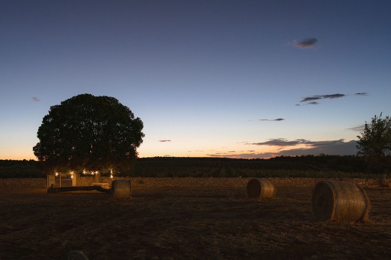Scenic sunset landscape with hay bales scattered across a rural field during golden hour.