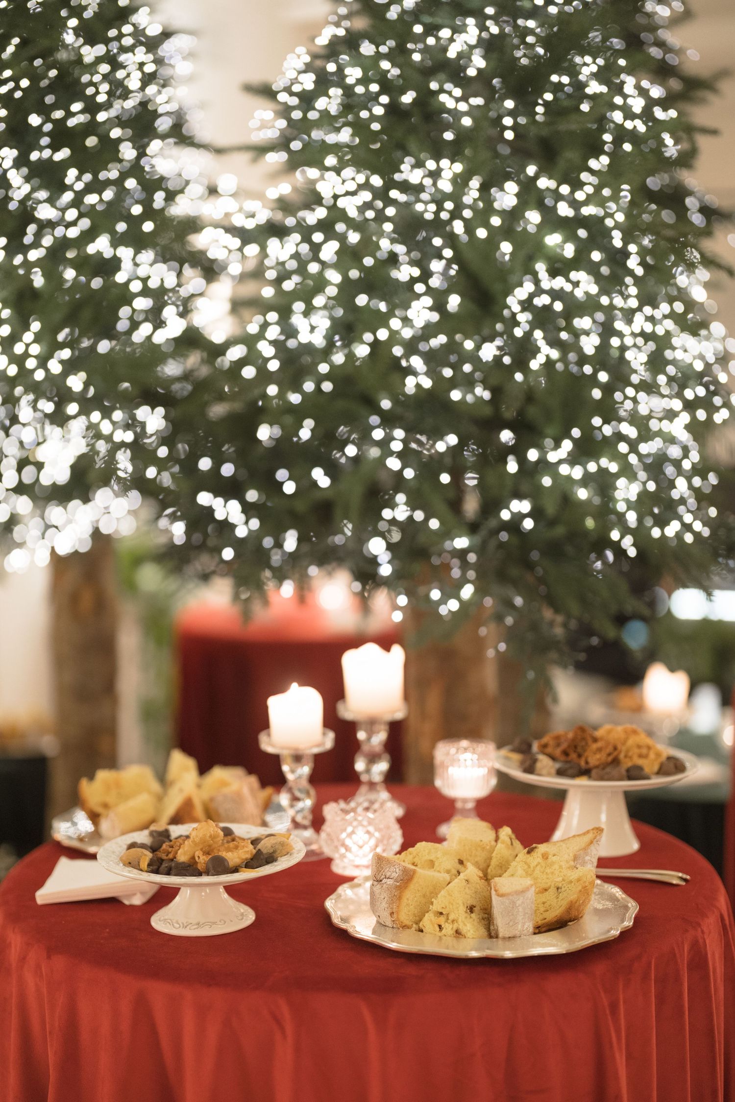 Festive wedding dessert table with candles and treats before a sparkling lit Christmas tree backdrop.