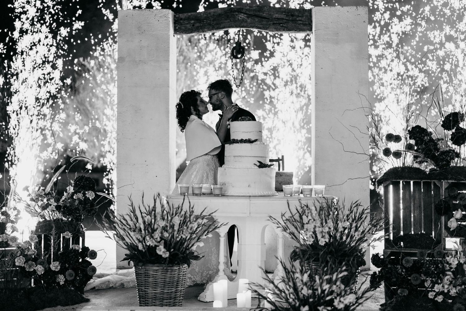 Bride and groom kiss behind wedding cake at outdoor ceremony in black and white photo.
