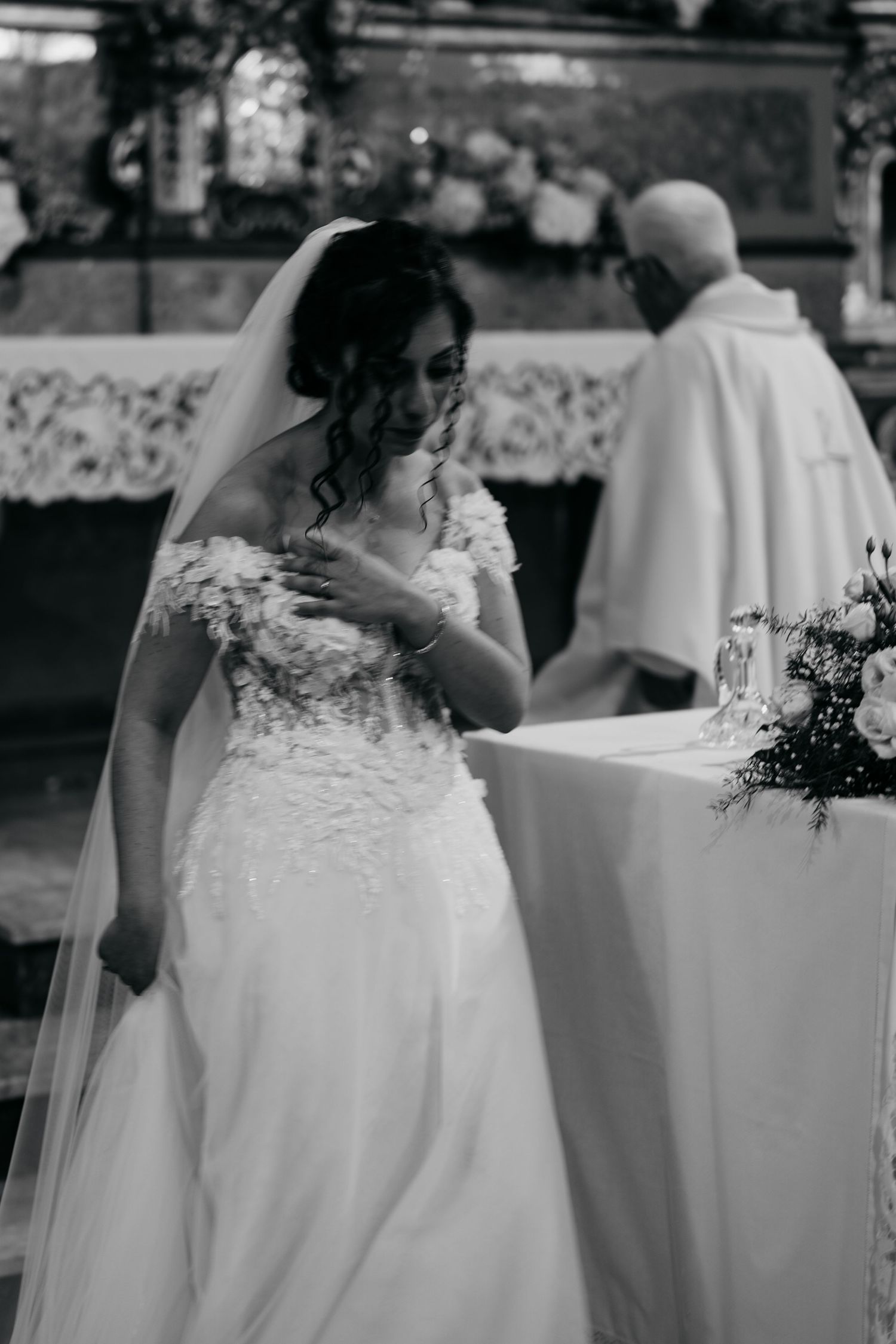 The bride in an intricately detailed lace wedding gown stands at the altar during a church ceremony.