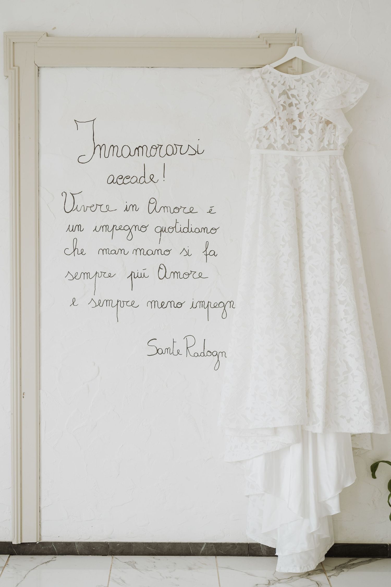 White lace wedding dress hanging beside Italian text written on a wall.