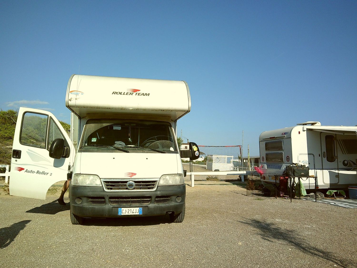 White motorhome parked in a camping area with other RVs visible.