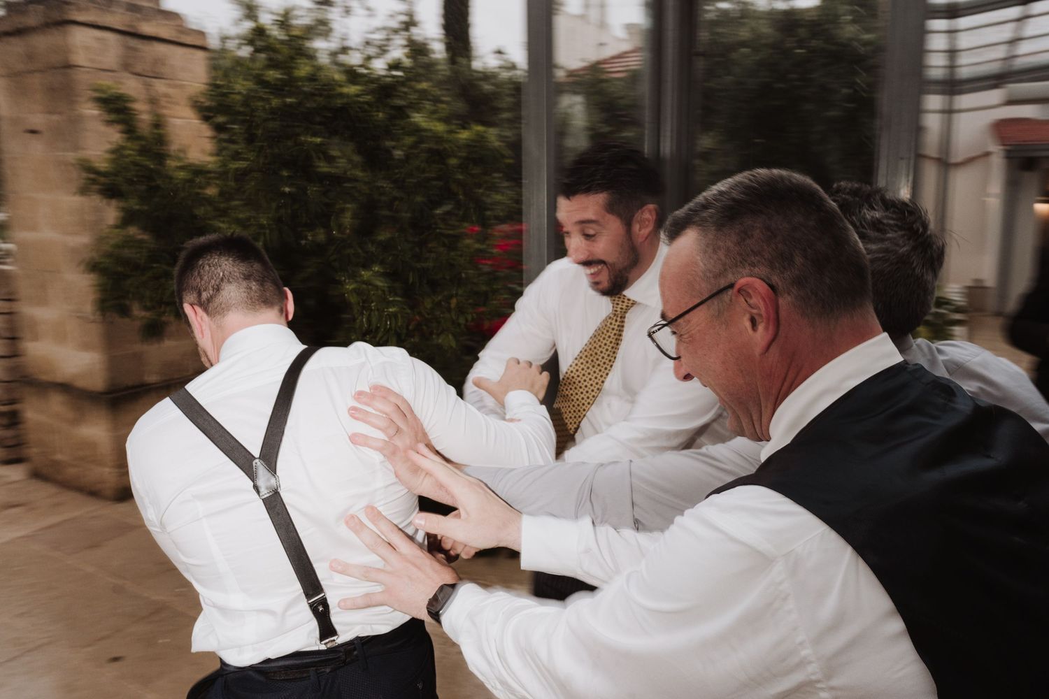 Men in white shirts and suspenders celebrating outdoors on a cloudy day.