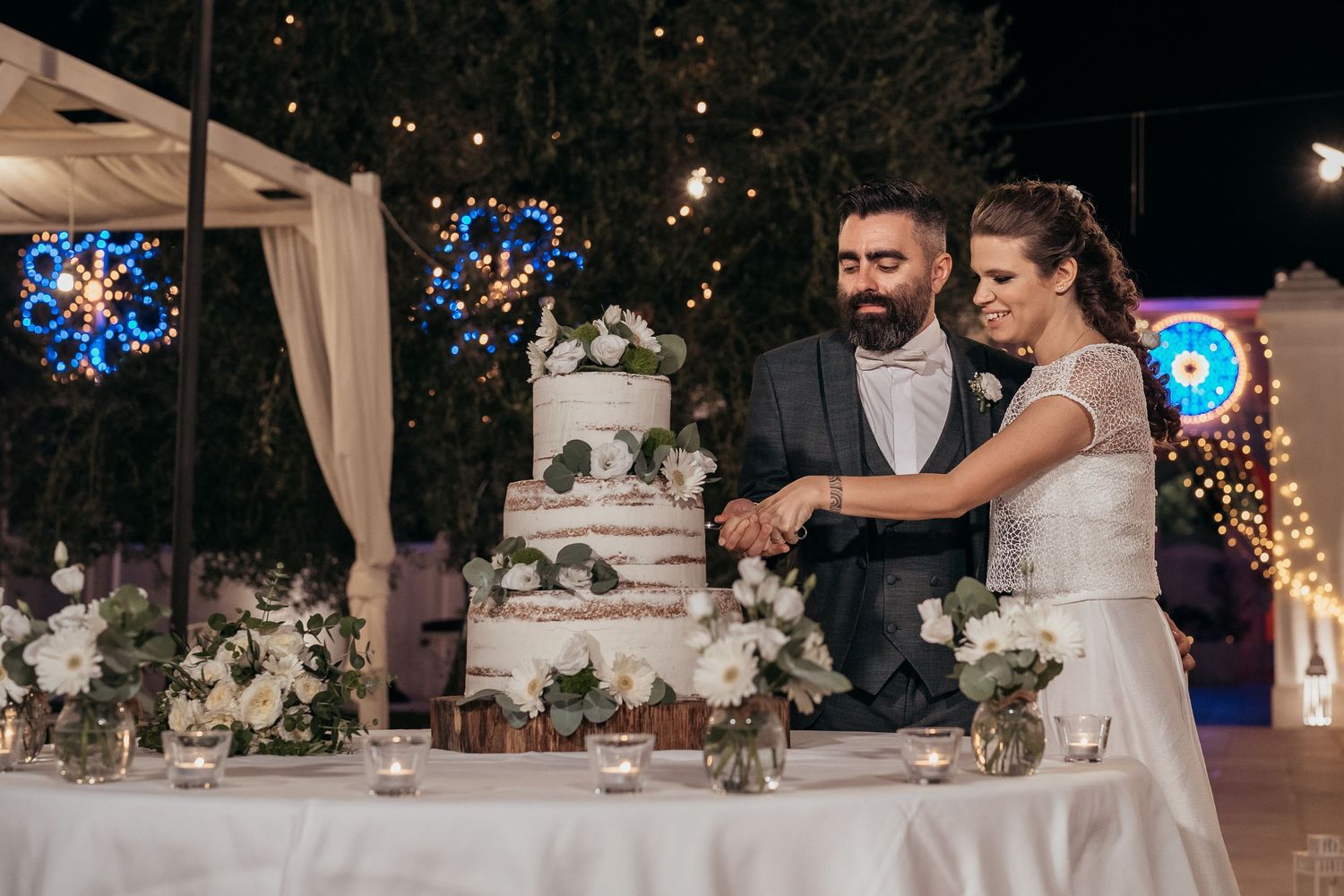 Wedding couple cutting their elegant white tiered cake decorated with flowers.