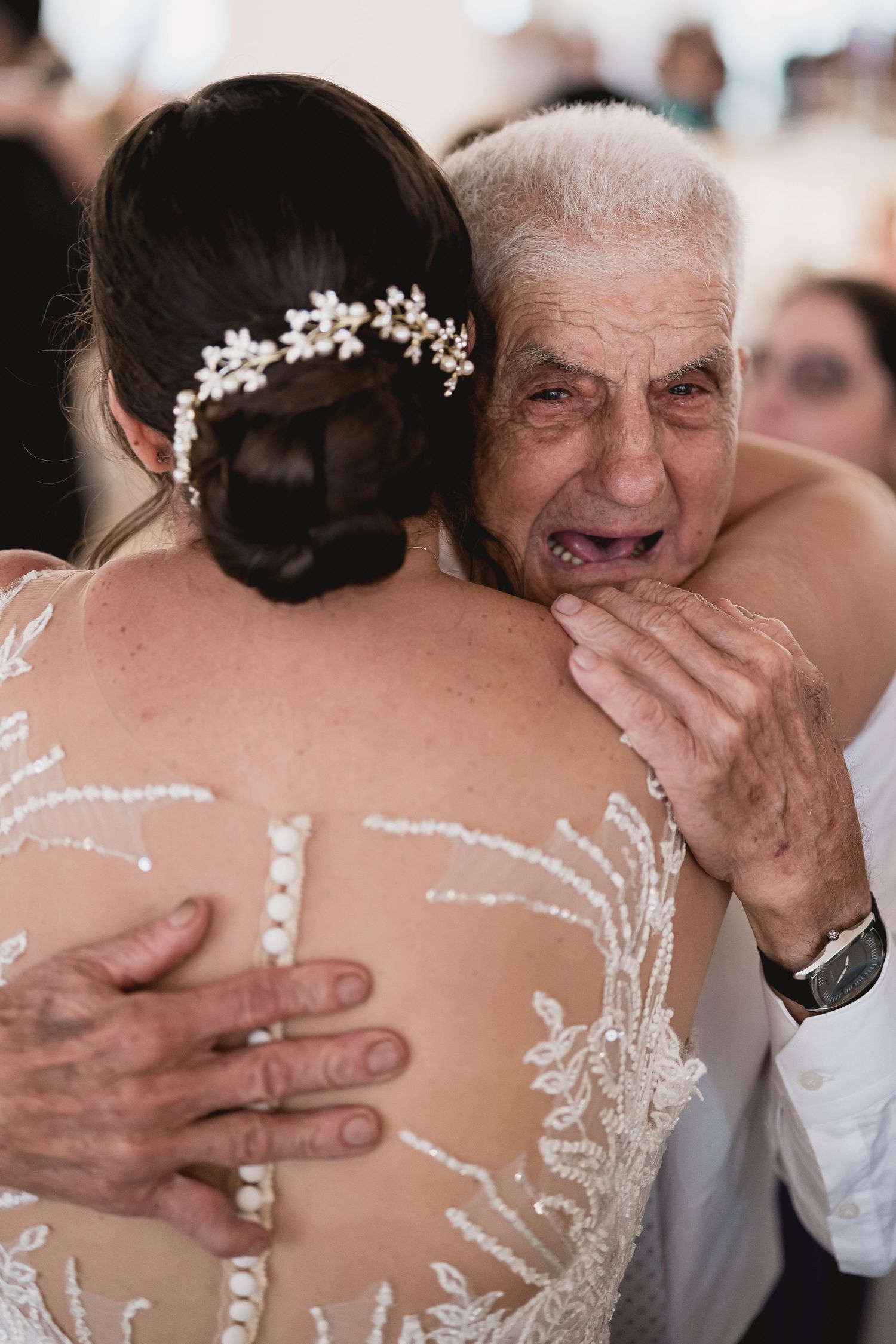 An emotional moment captured during a wedding dance showing the back of a bride's detailed lace dress.