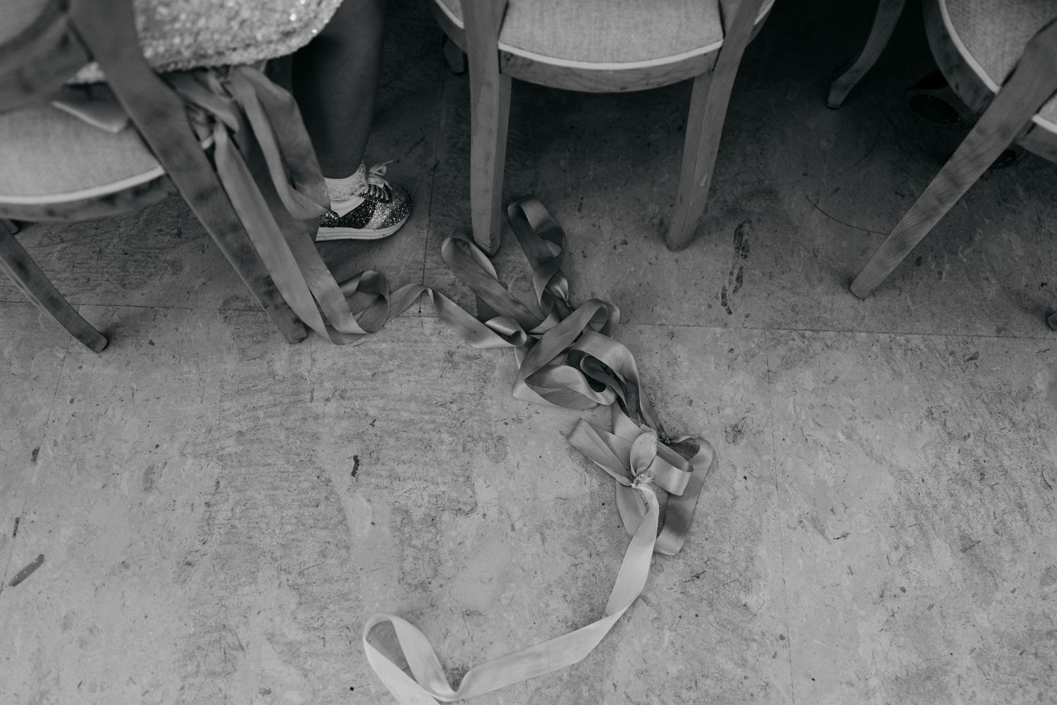 Black and white detail shot of ribbon on floor between wedding reception chairs.