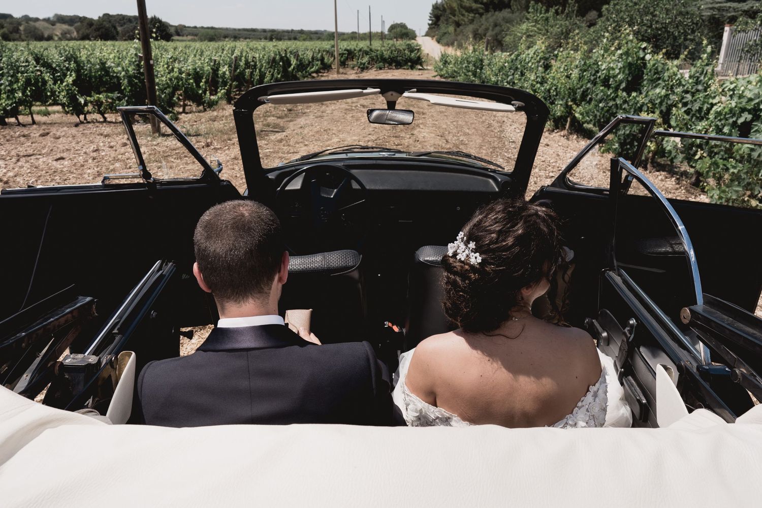 Couple riding in vintage convertible car through countryside on sunny day.