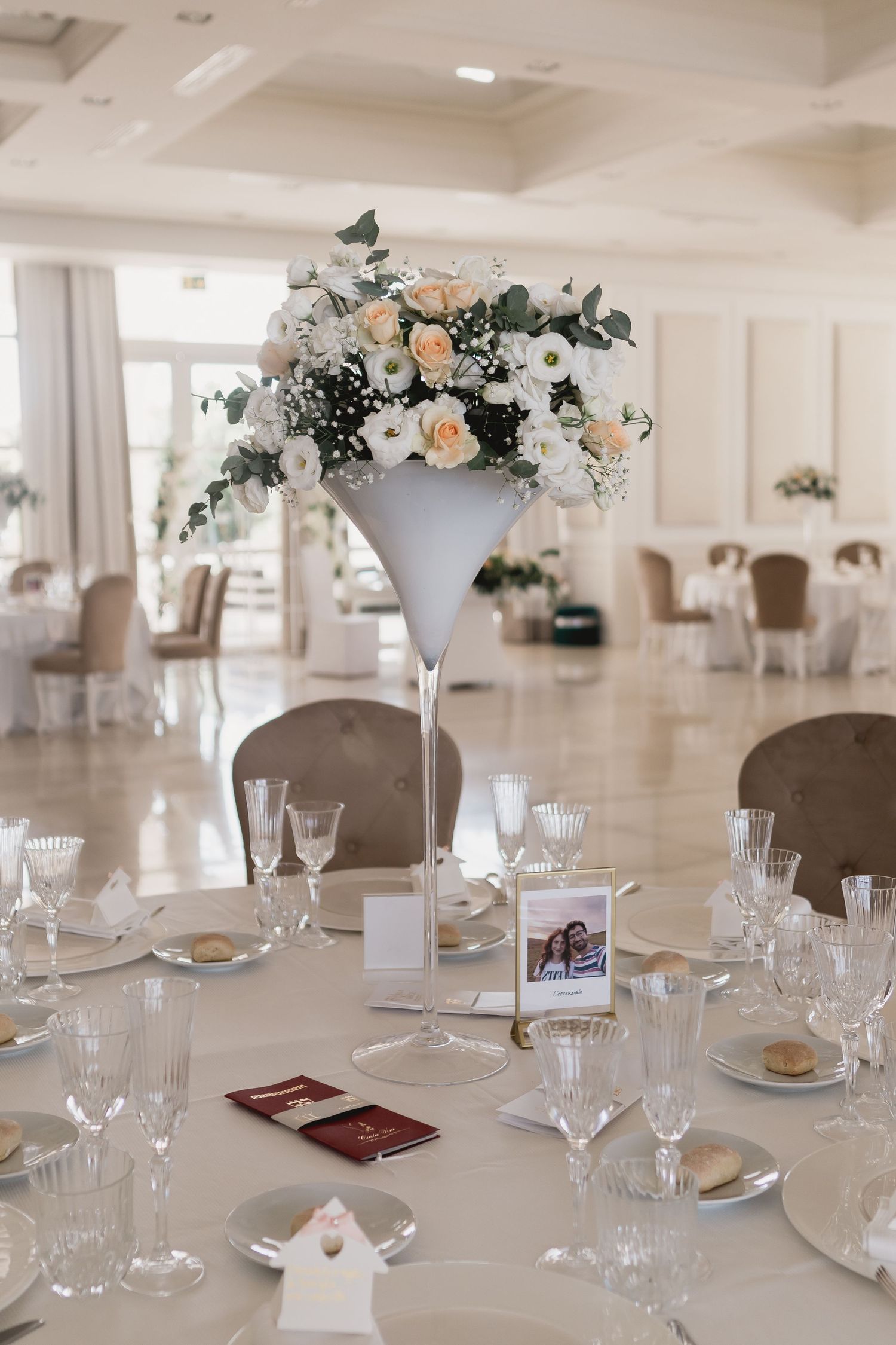 Elegant wedding reception table with tall martini glass centerpiece filled with peach and white flowers.