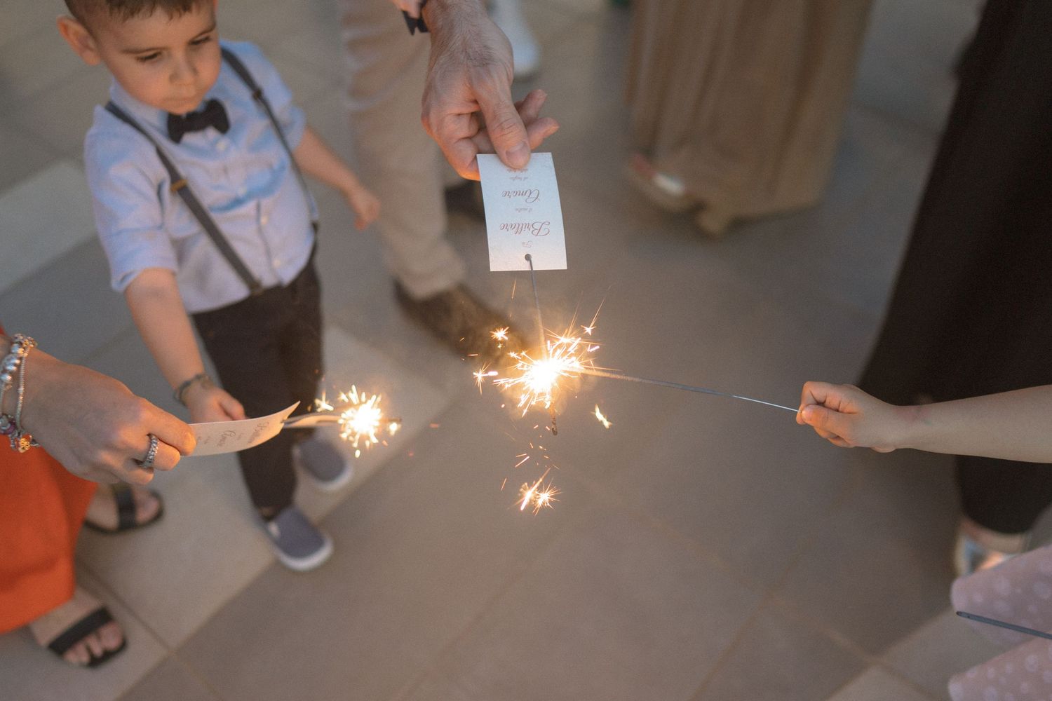 Small sparklers being lit during a wedding celebration with guests holding them.
