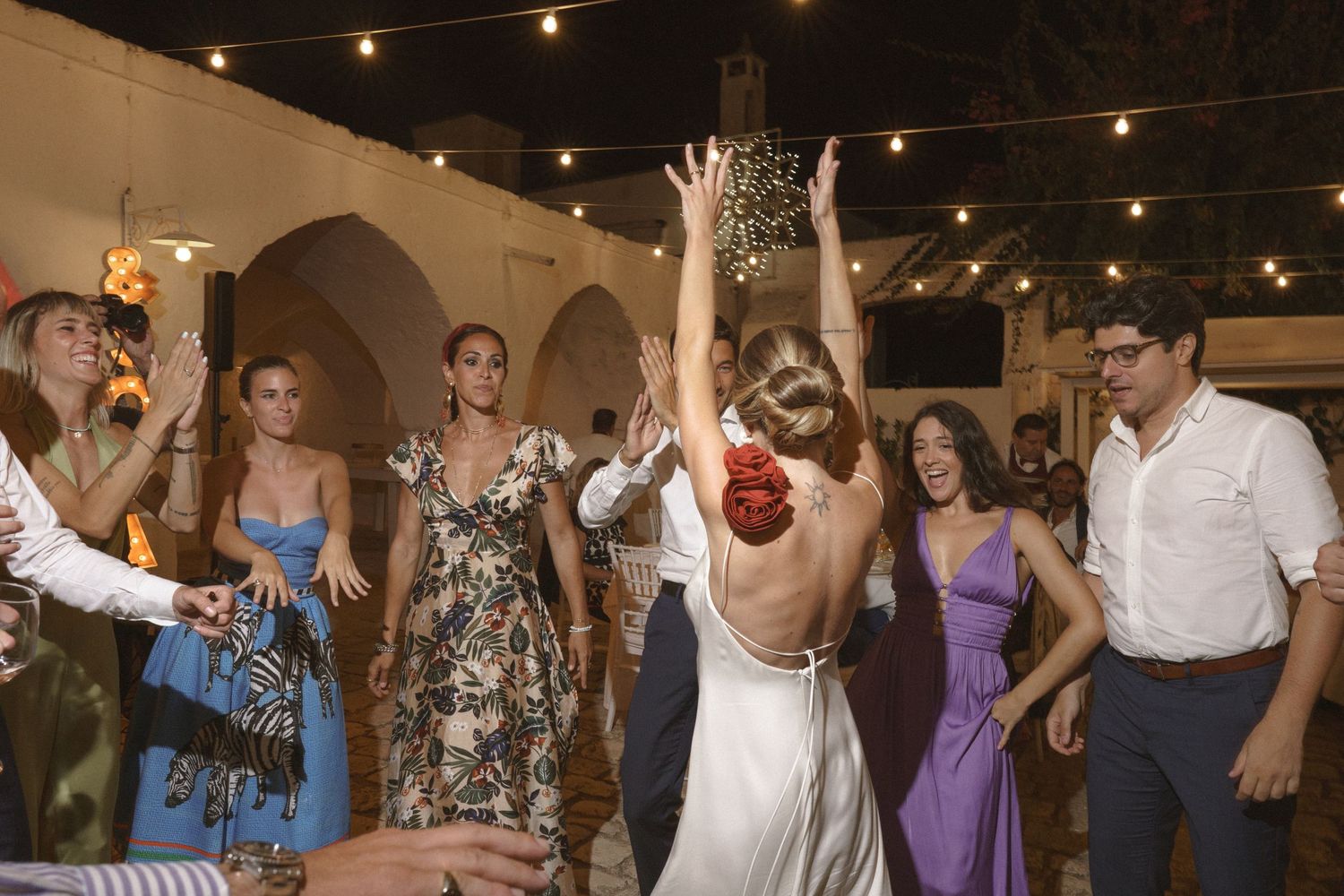 Wedding reception guests dancing and celebrating under string lights in an indoor venue.