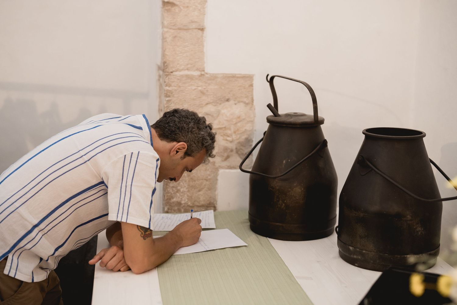 Someone writing at a table with vintage metal milk cans displayed beside them.