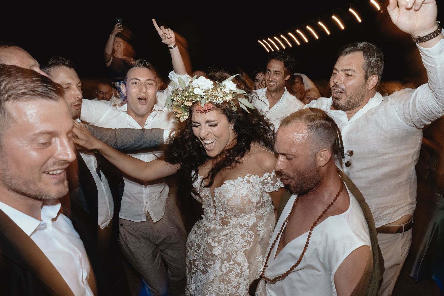 Bride wearing a floral crown dances joyfully with wedding guests at a lively reception celebration.