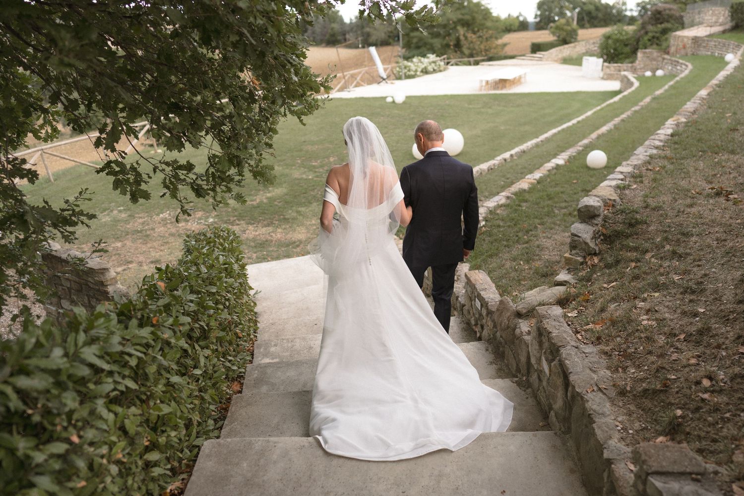 A wedding couple walks along a stone path surrounded by green landscaping.