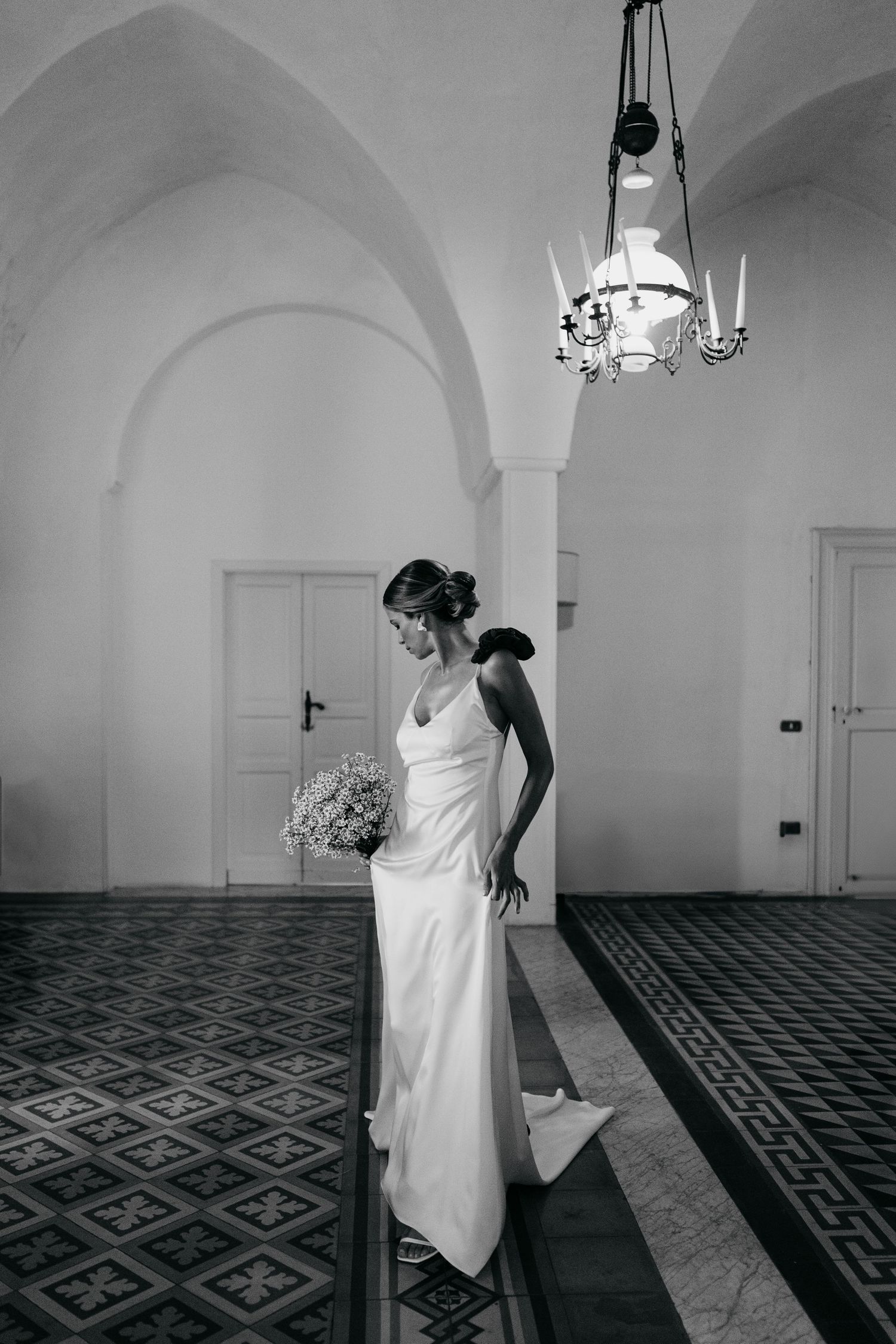 A figure in a white dress performs an expressive dance sequence across a geometric patterned floor in black and white.