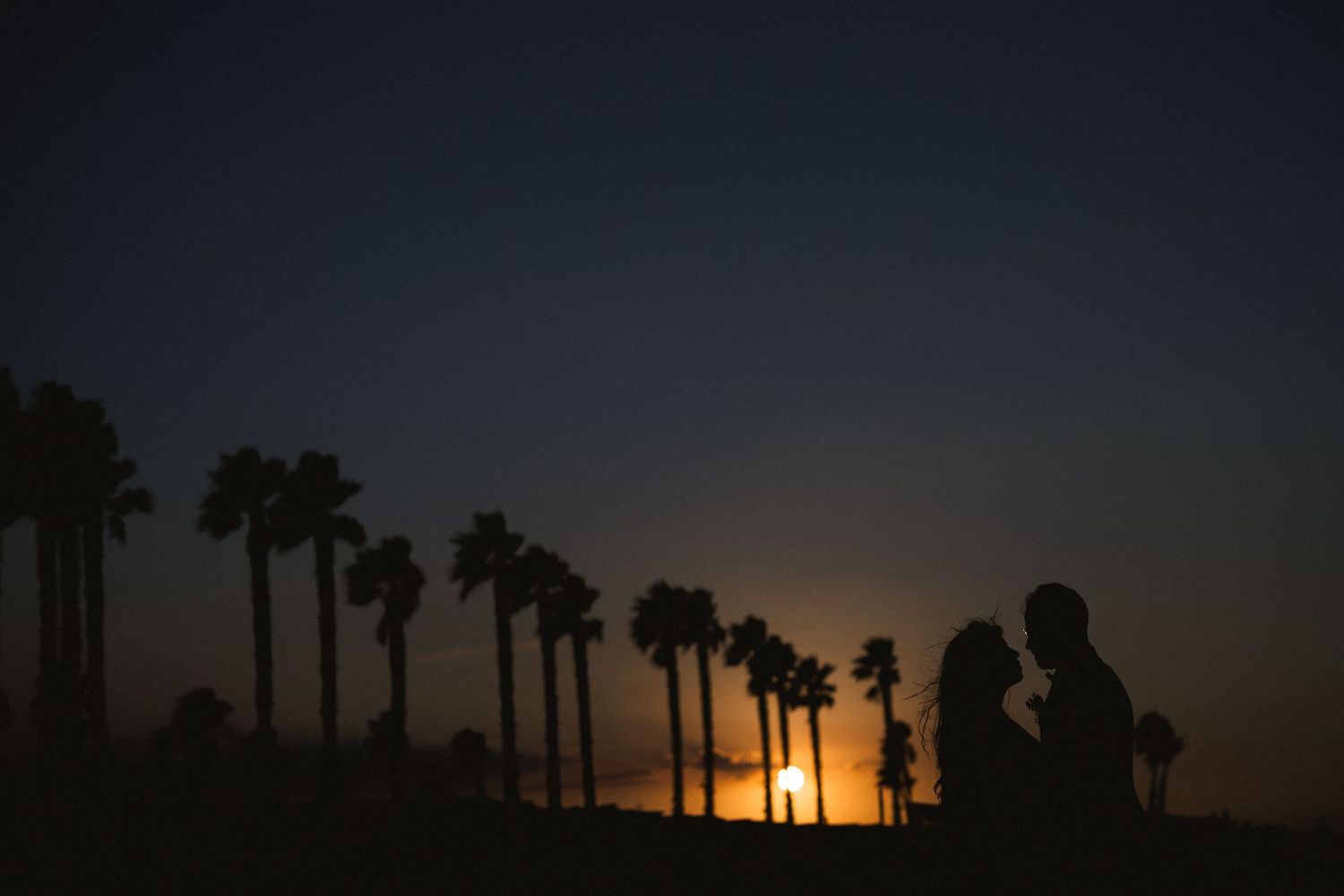 Silhouette of a couple against sunset with palm trees in the background.