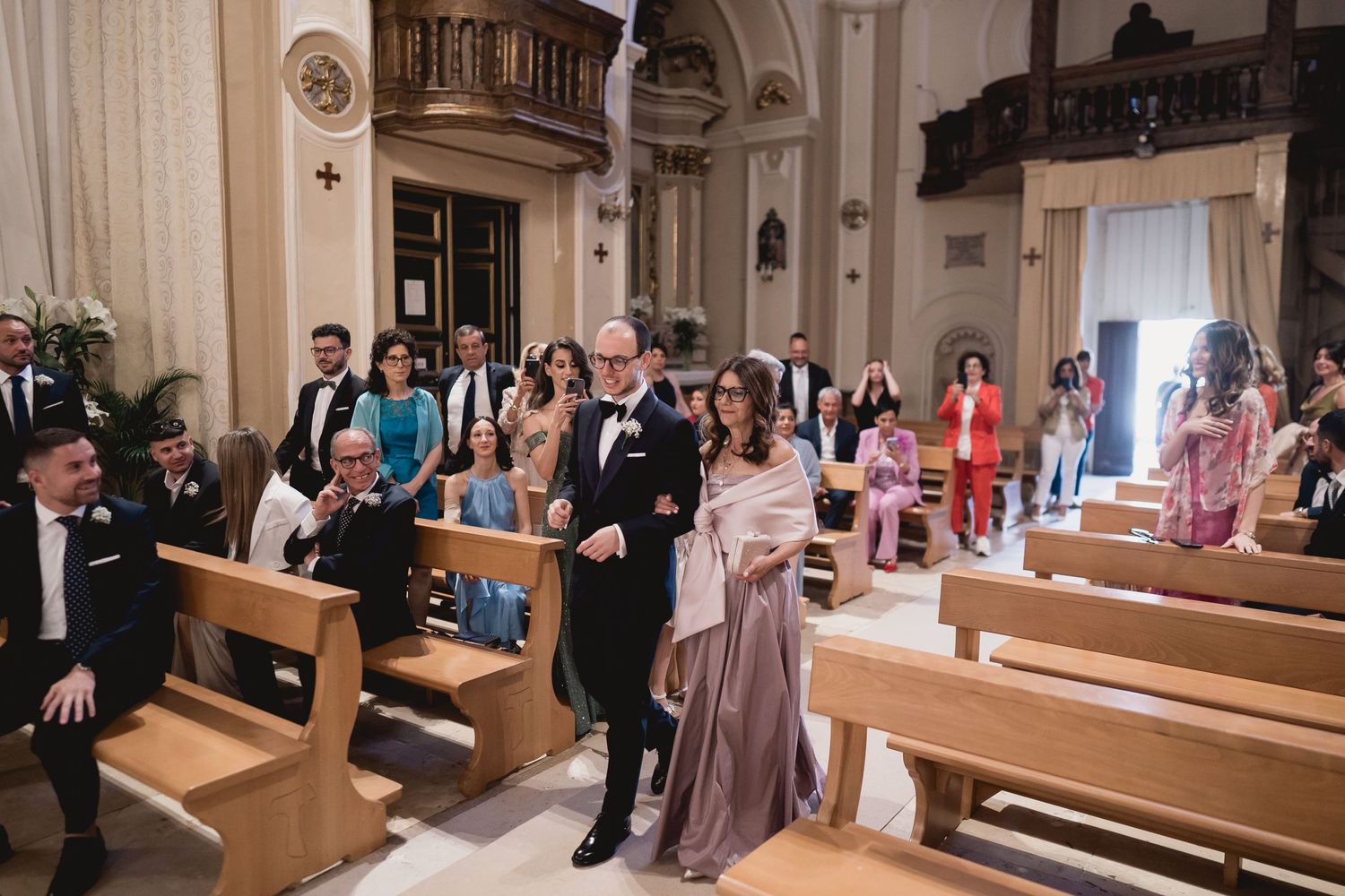 Wedding guests seated in wooden church pews during ceremony.