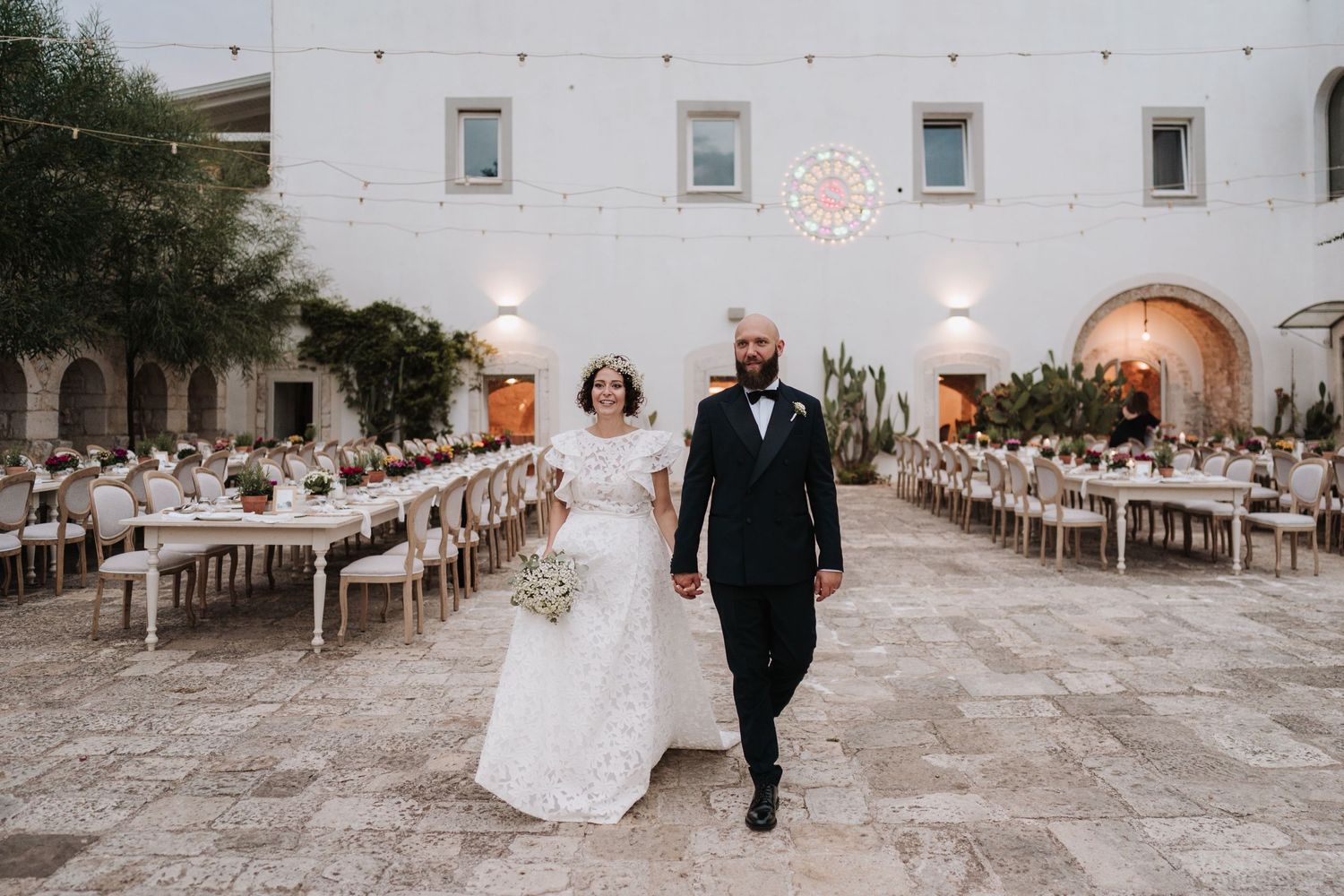 A newlywed couple walks through an elegant white courtyard set up for a wedding reception.