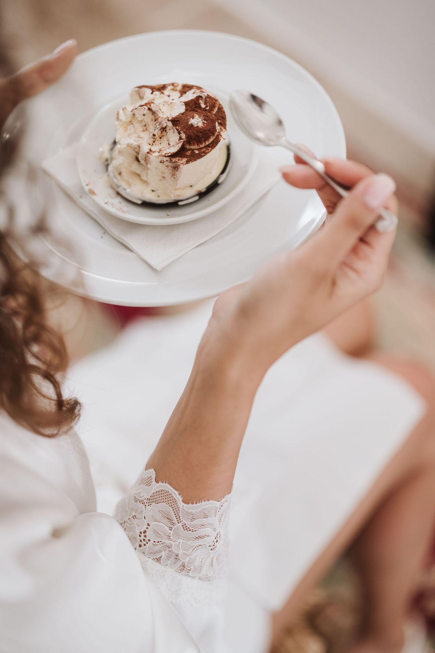 A delicate dessert with whipped cream served on a white plate being enjoyed by someone in lace.
