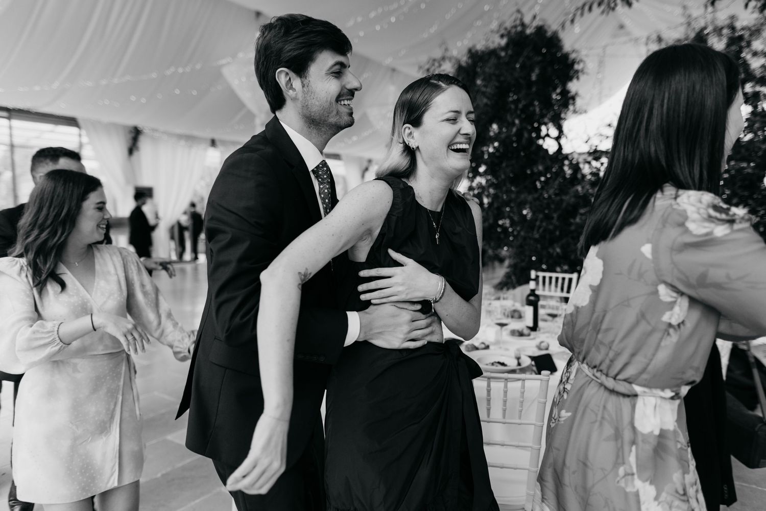 Wedding guests dancing and laughing together under white tent.
