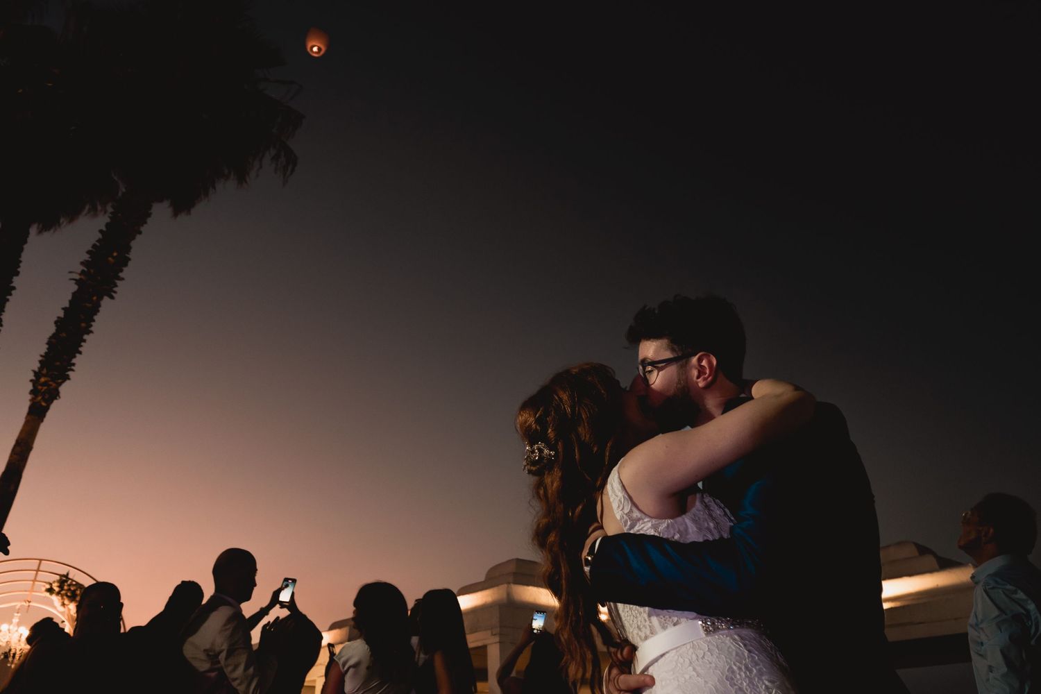 Silhouettes of a dancing crowd at sunset with palm trees in the background.