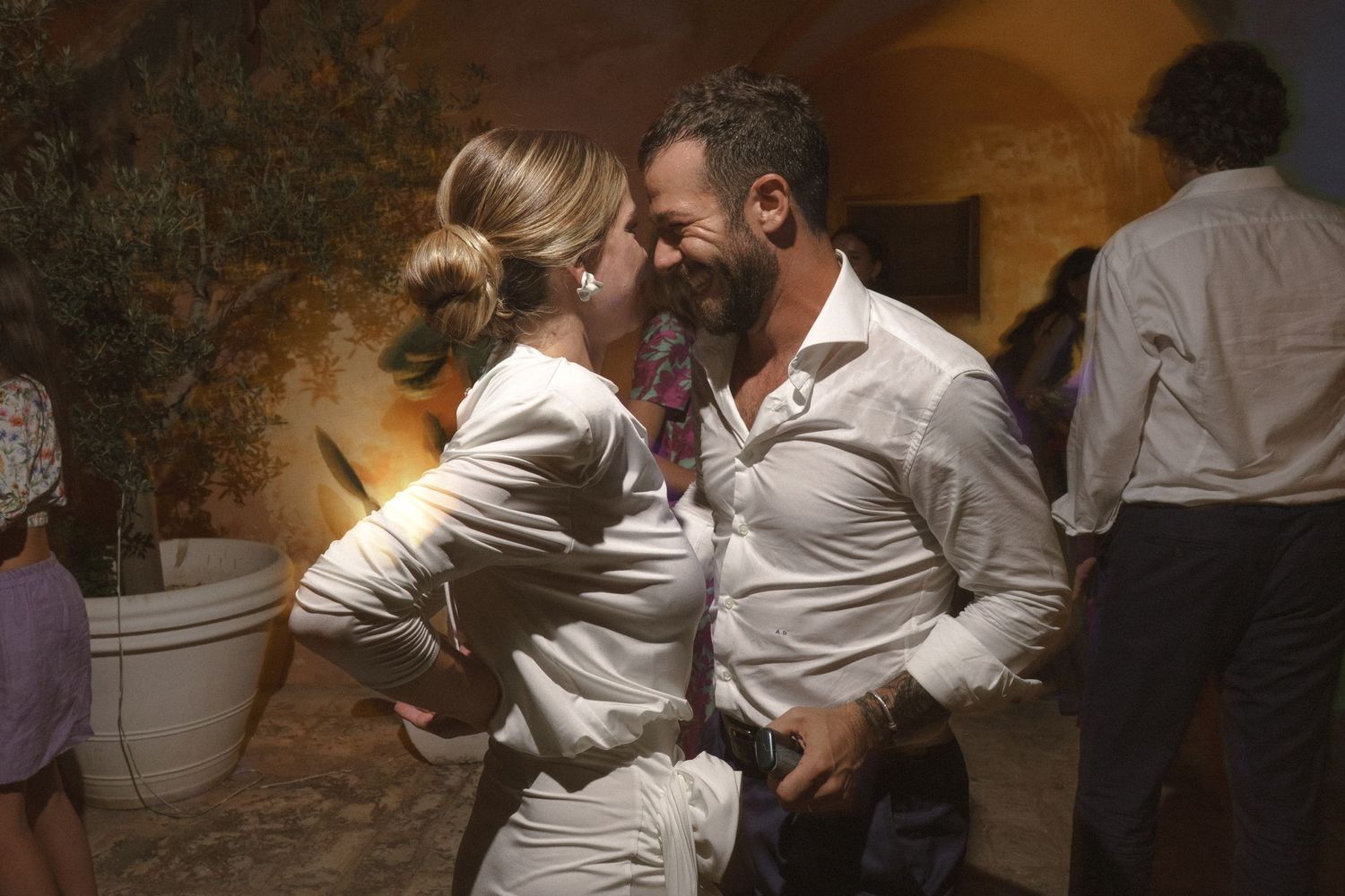 A couple in white outfits share a romantic dance moment in a dimly lit venue with atmospheric lighting.