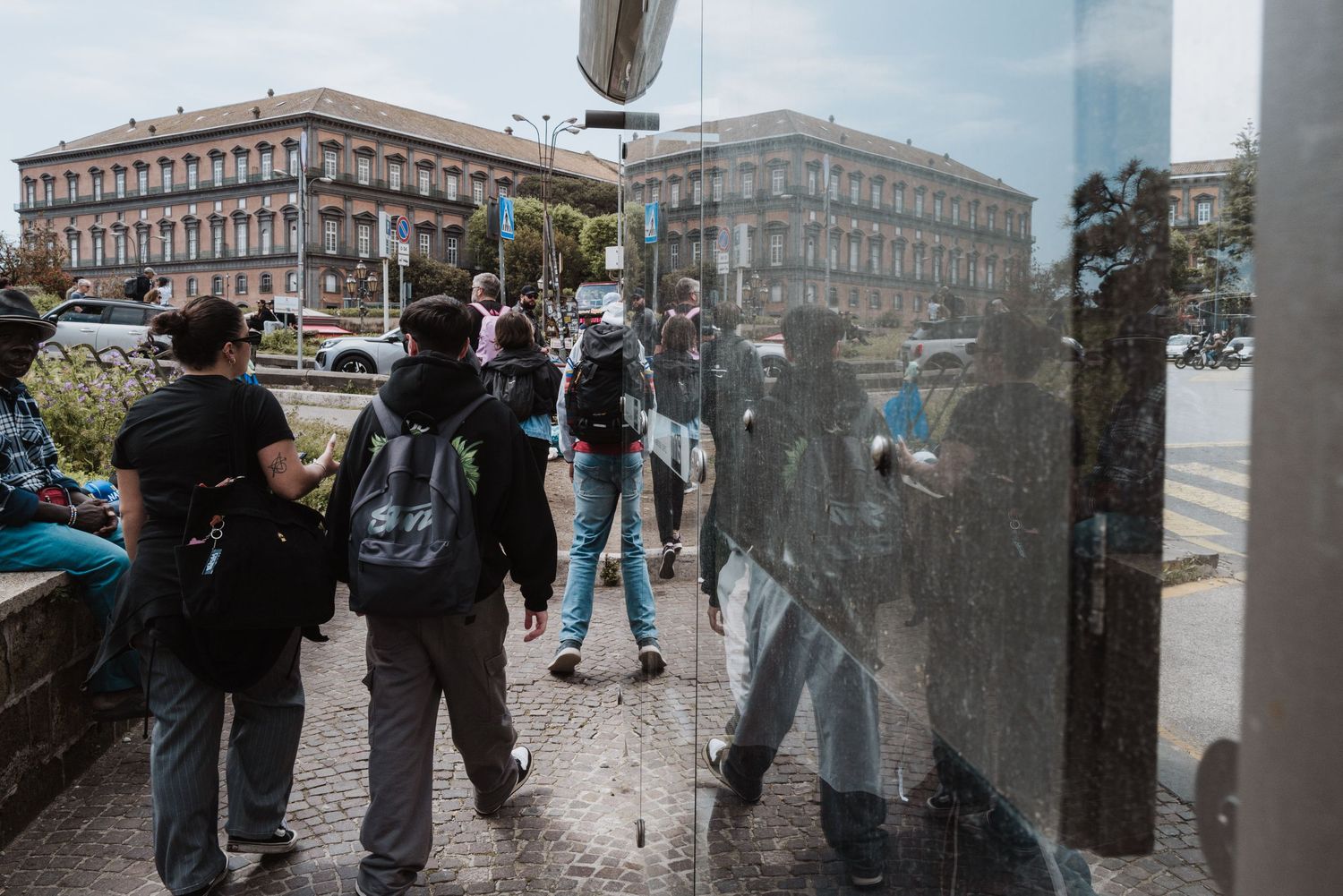Protesters with backpacks face off with police through glass reflections during an urban demonstration.