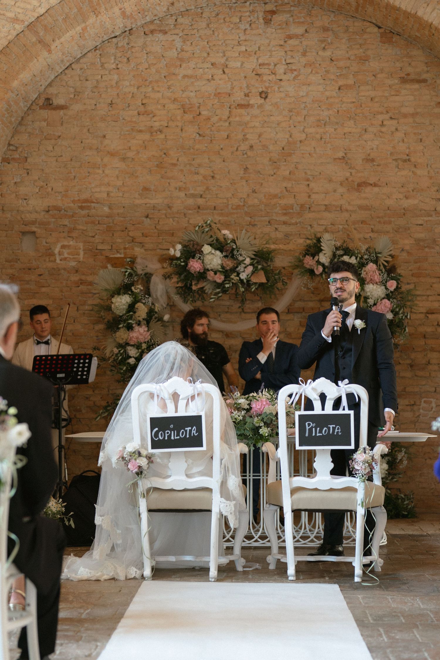 Wedding ceremony setup with white chairs and chalkboard signs in a rustic brick venue.