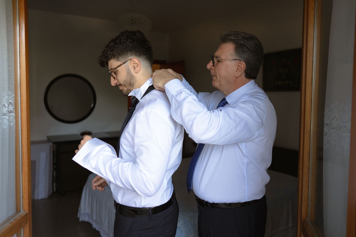 Three men in white dress shirts are seen adjusting their bow ties in a mirrored reflection.