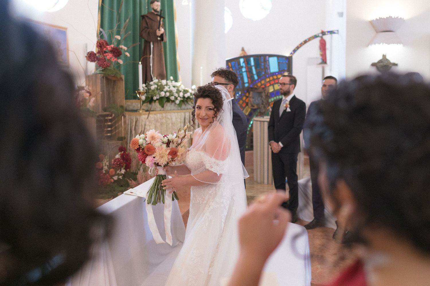 Bride in white gown holding bouquet walks down church aisle at wedding ceremony.