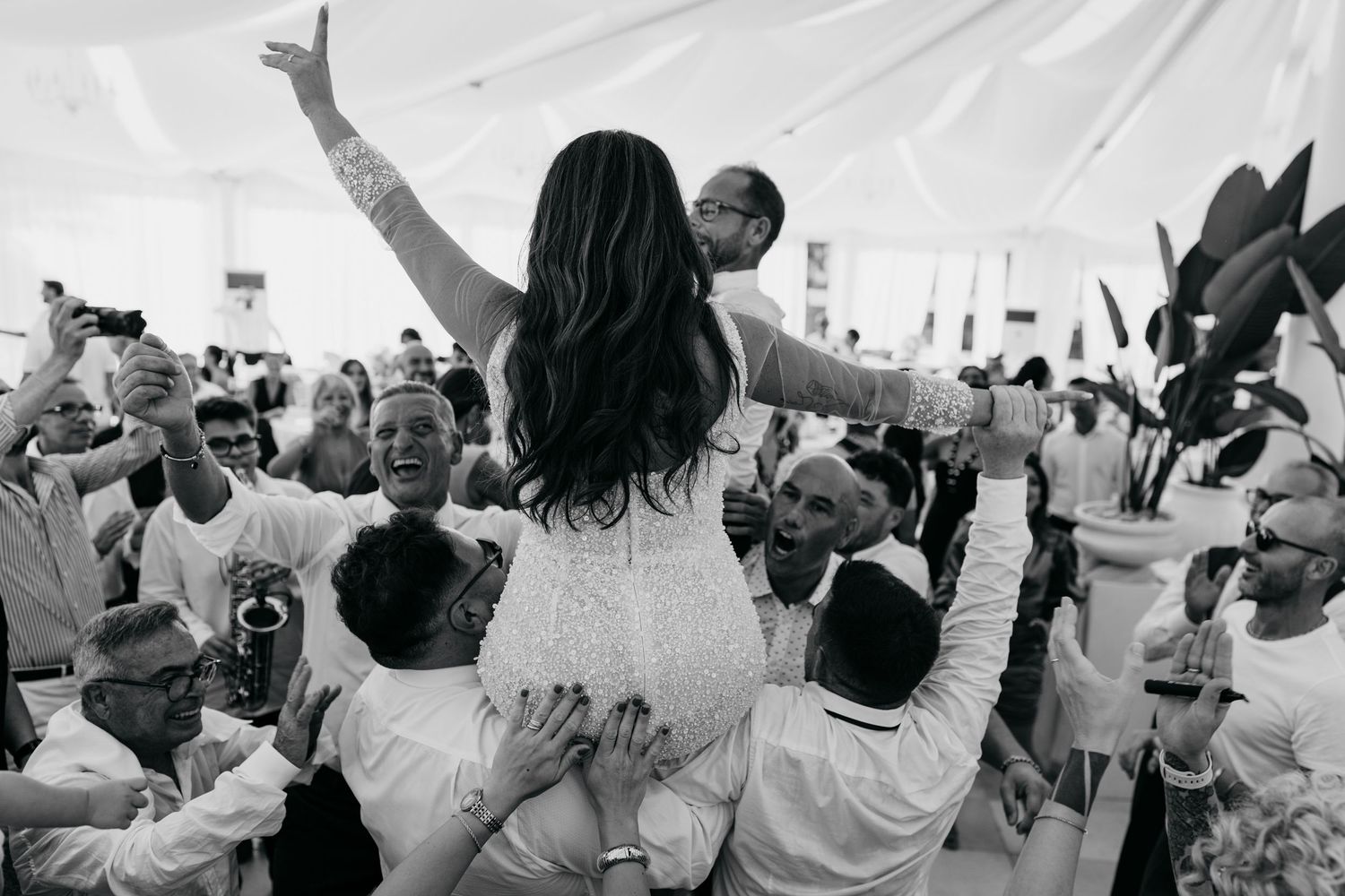 A large crowd of people with raised arms celebrating at an outdoor event with white tents visible.