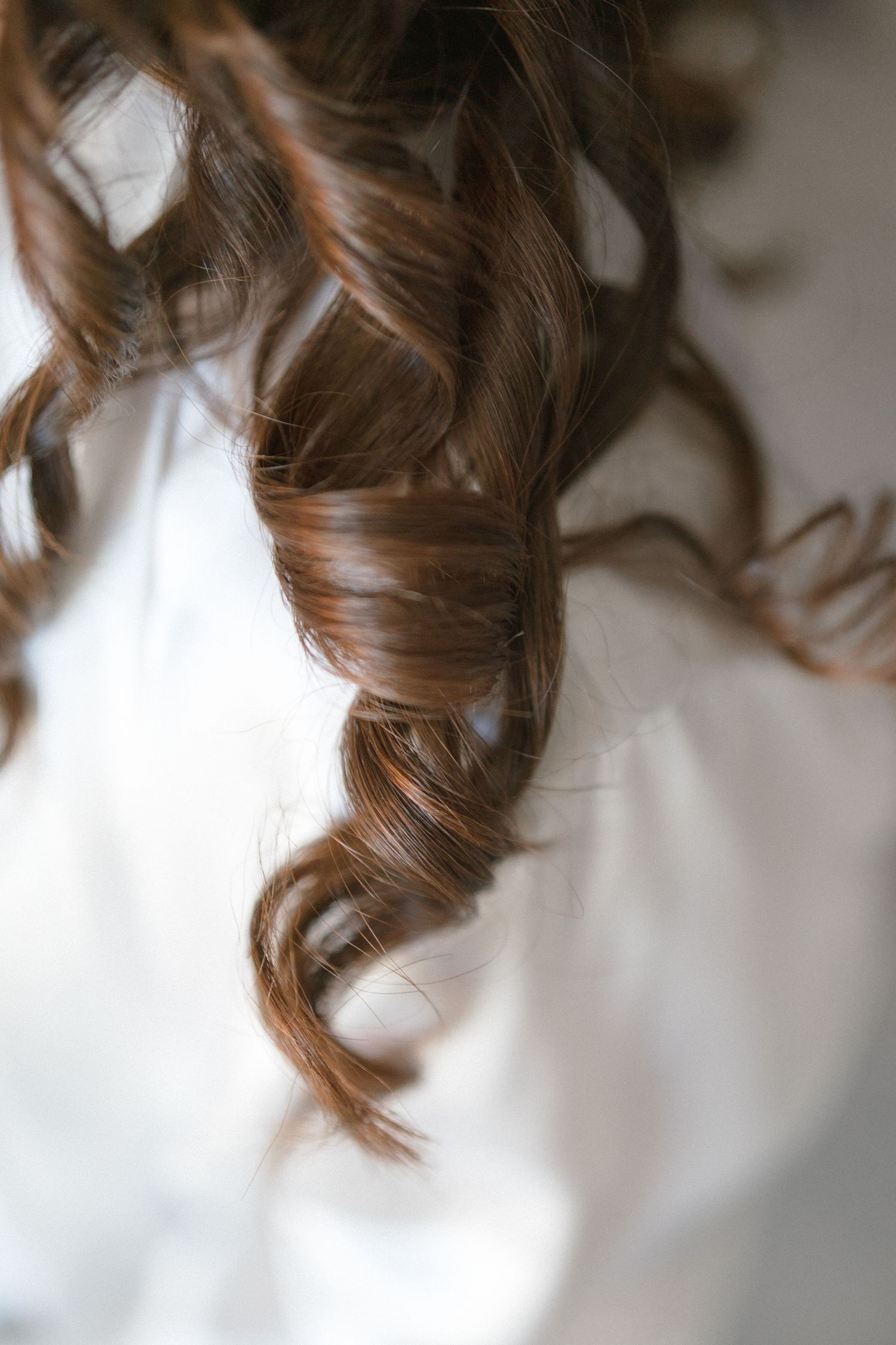 Close-up of cascading brown curled hair against a white background.