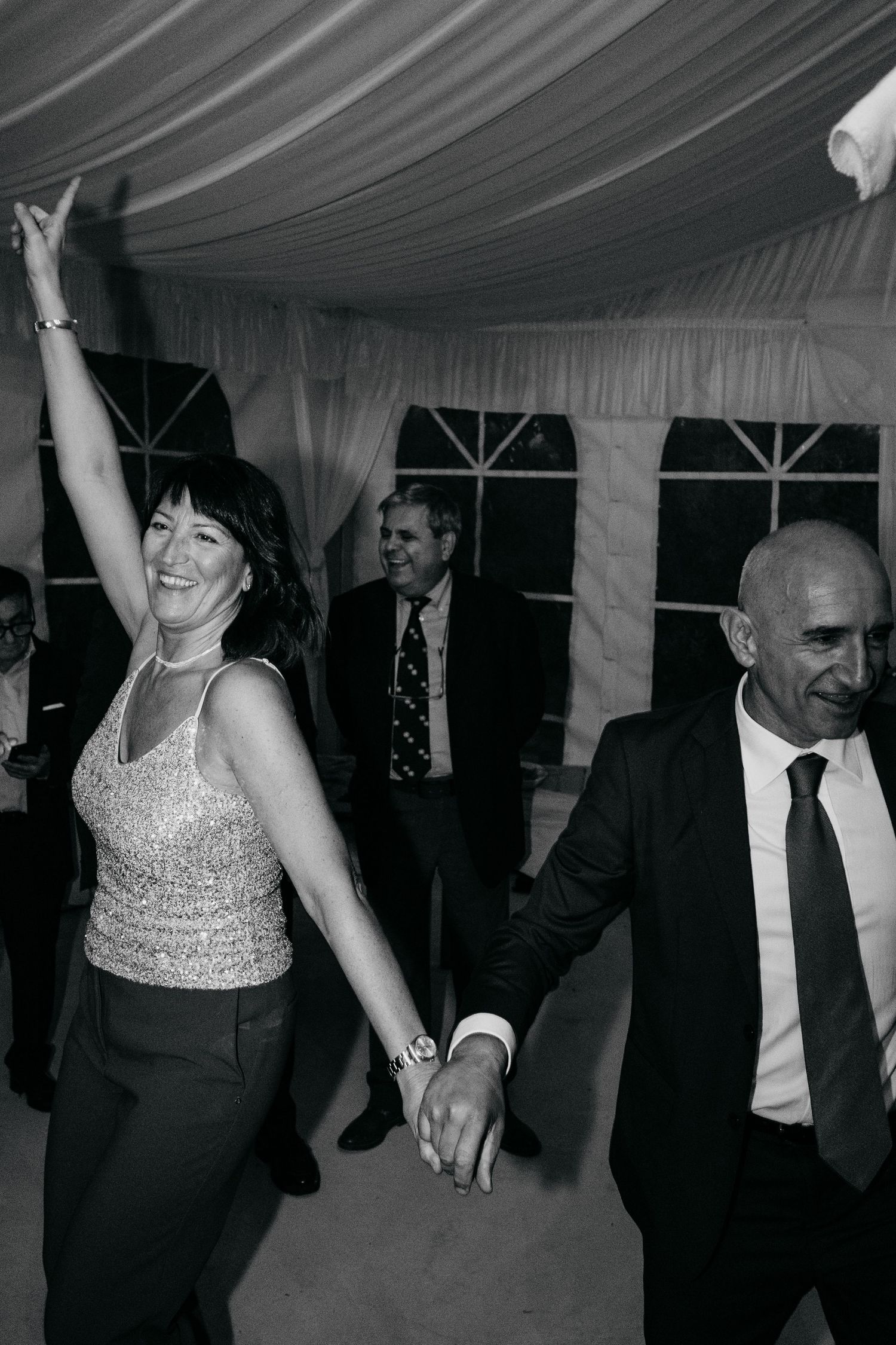 Wedding guests dancing and celebrating on the dance floor under a white tent at an evening reception.