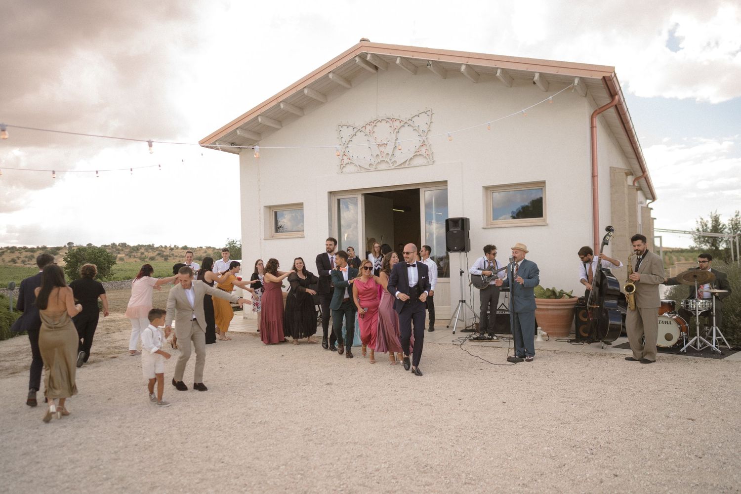 Wedding guests gather outside a white stucco building under cloudy skies.