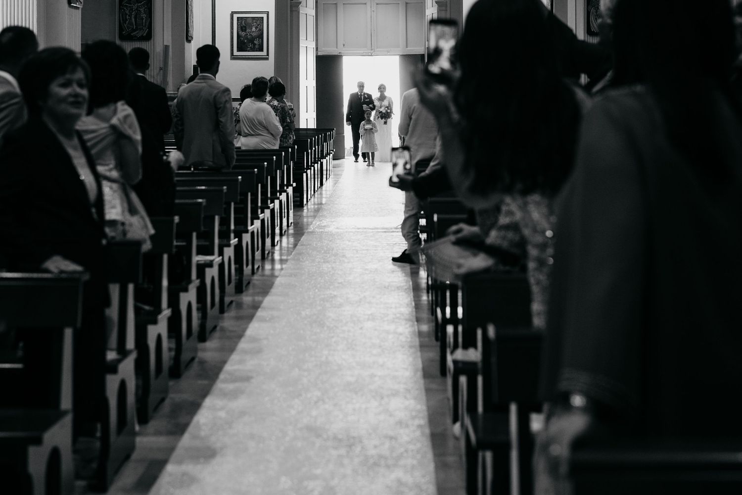 Dark silhouette of wedding guests seated in church pews during ceremony.