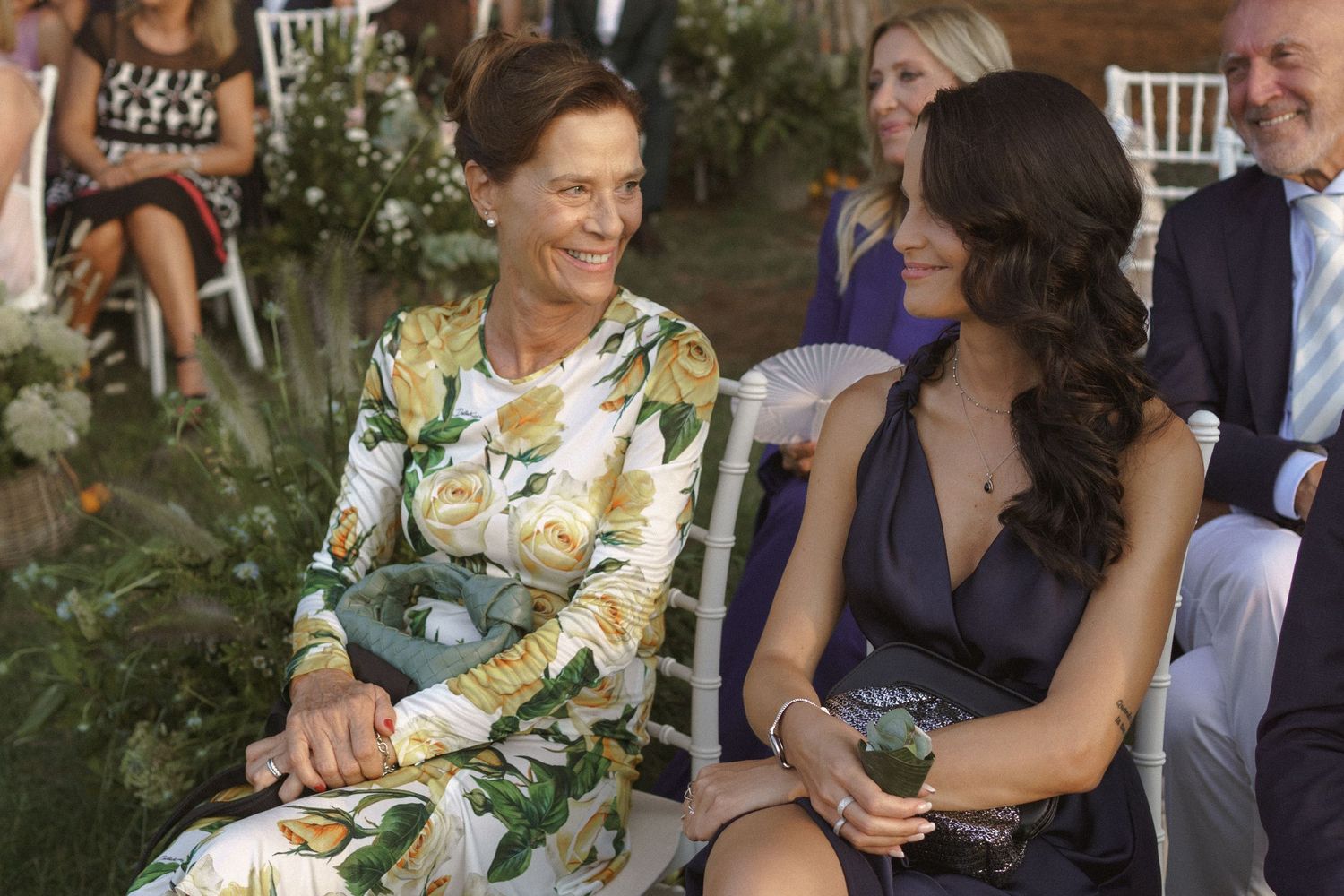 Wedding guests seated outdoors in elegant attire during a garden ceremony.