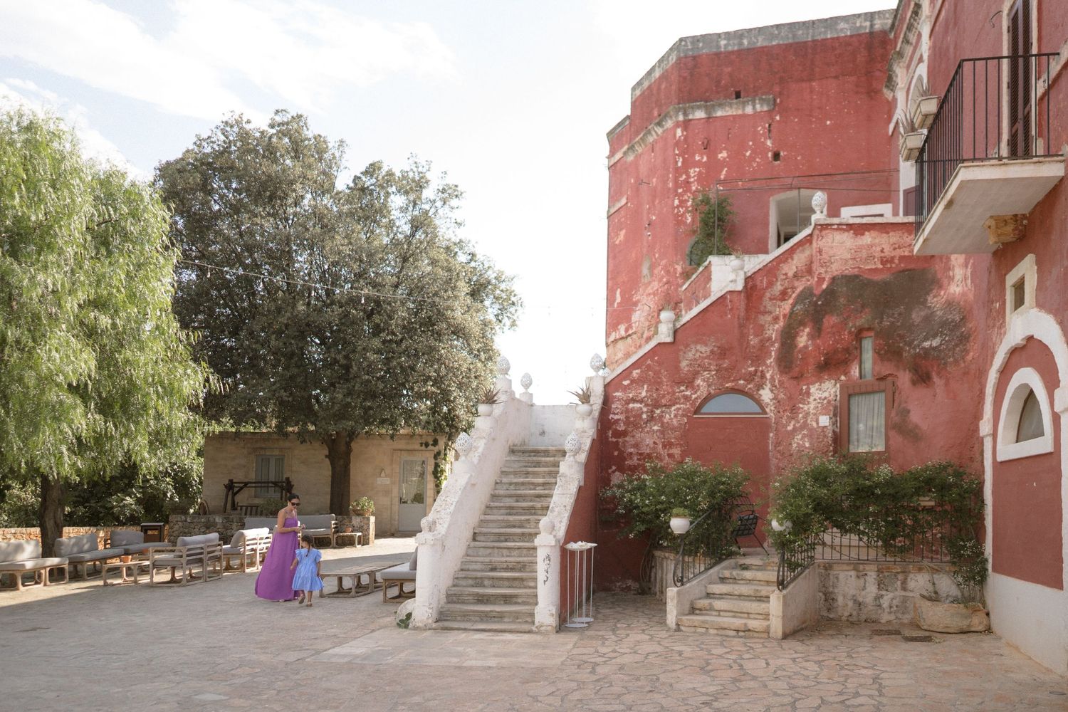 Exterior view of a rustic red building with stone steps and Mediterranean architecture.