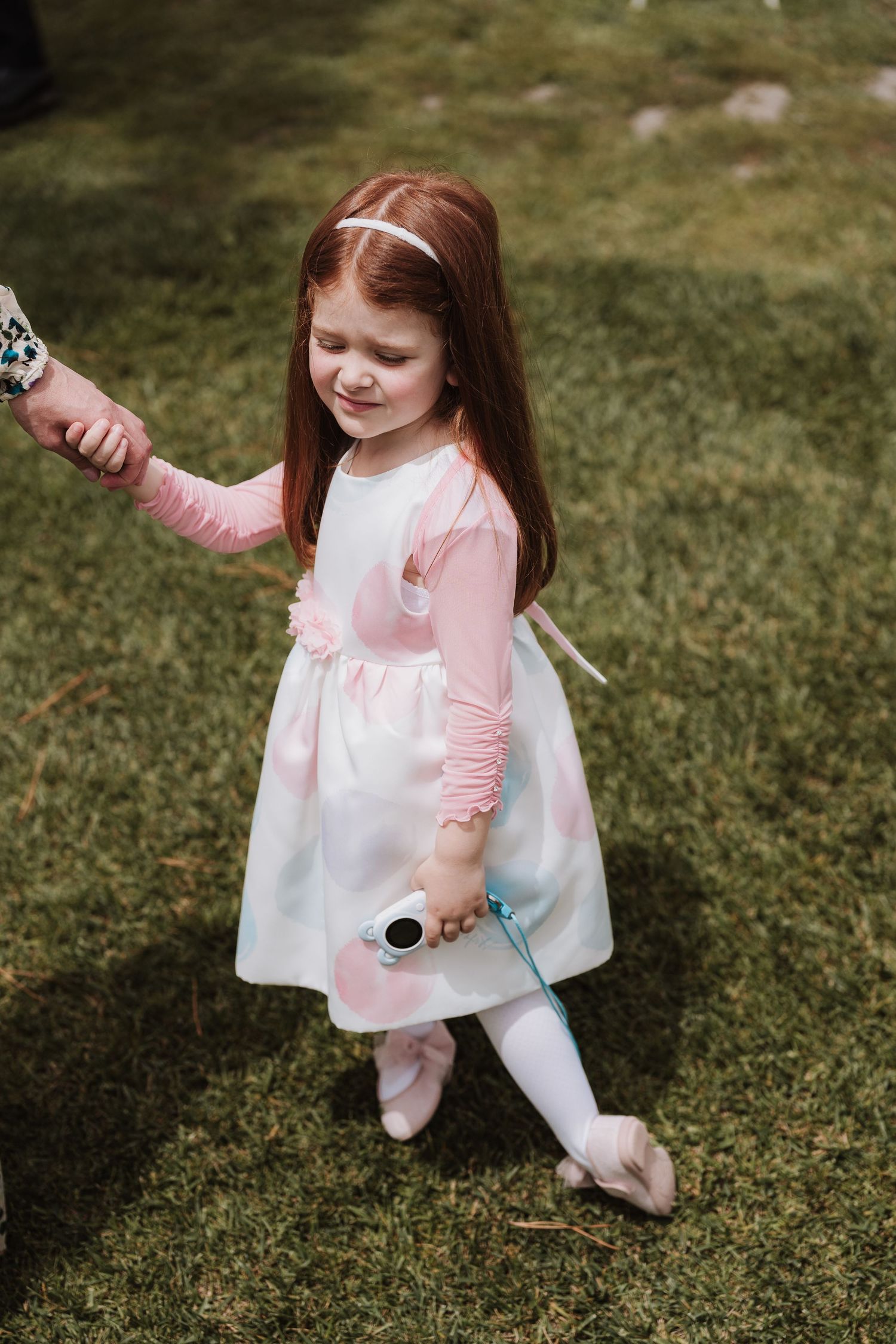Young girl in white and pink dress and tights playing on grass at event.