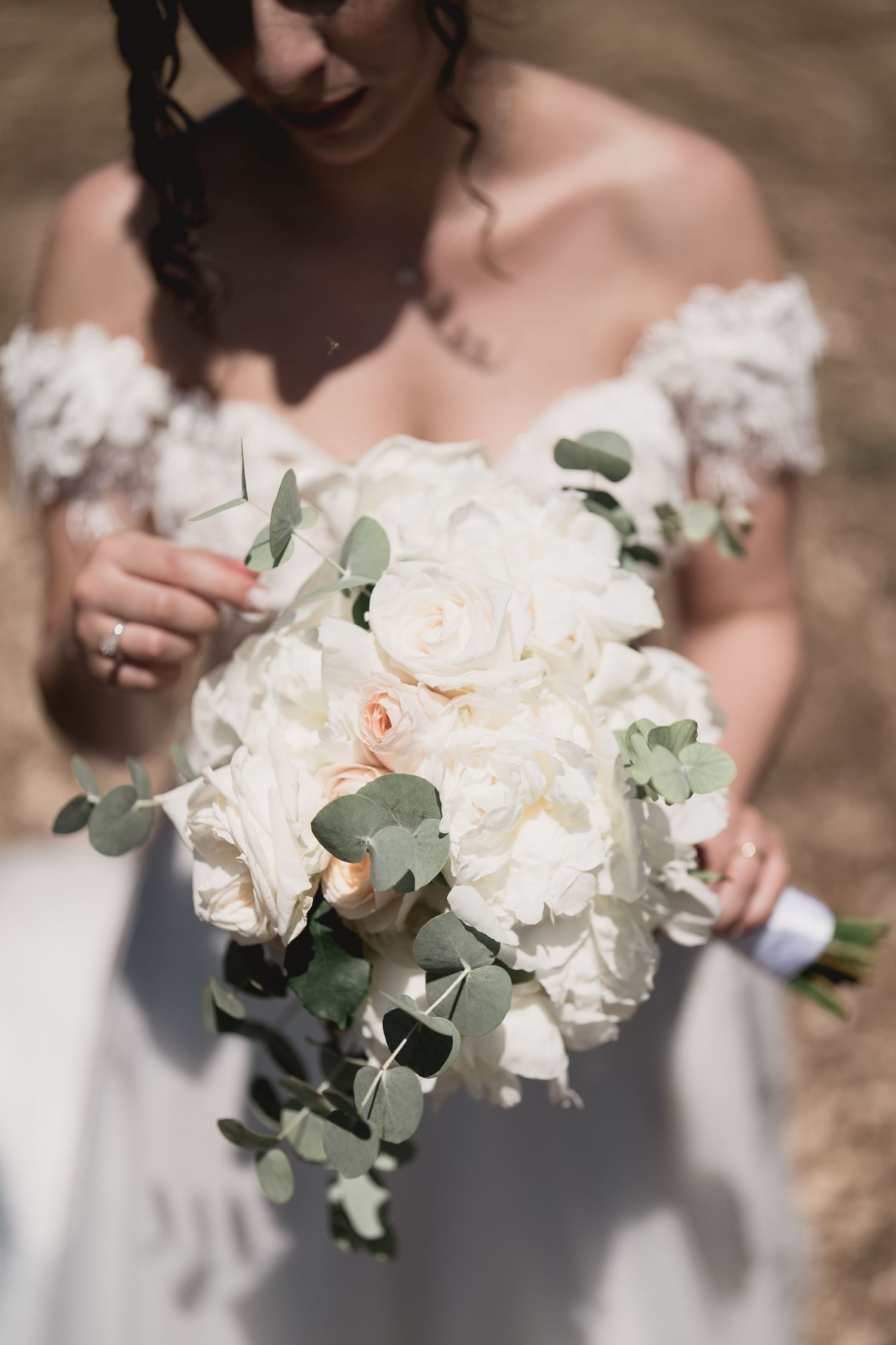 Elegant white bridal bouquet with roses and eucalyptus leaves held against a wedding dress.