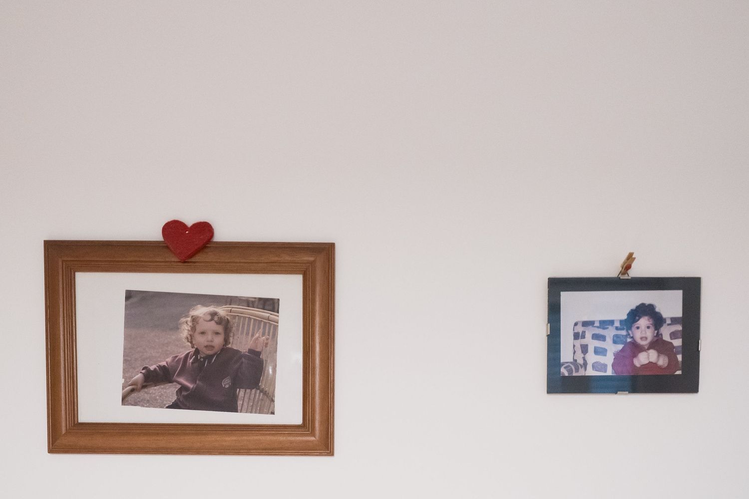 Two framed photographs hang on a white wall with a small red heart decoration.
