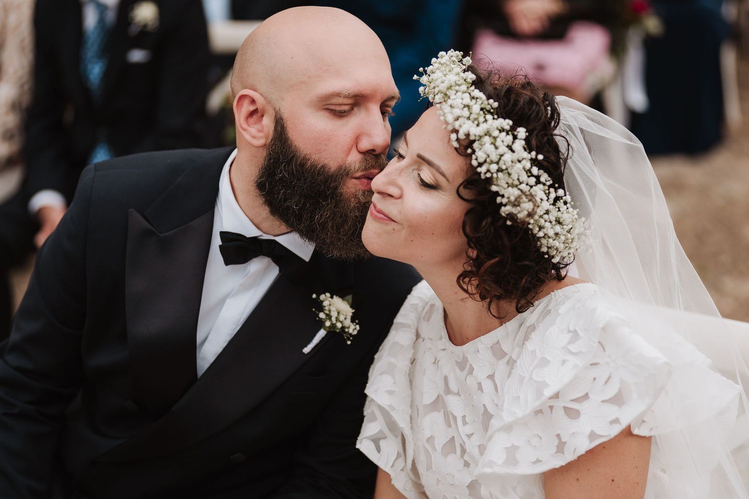 Intimate wedding moment captured as couple shares tender kiss under floral crown.