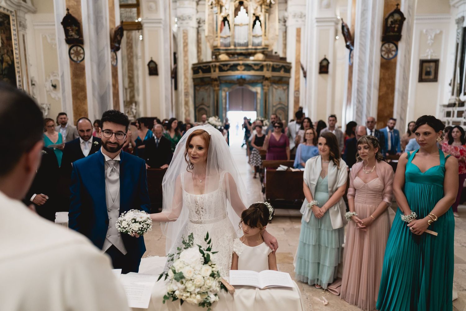 Wedding ceremony in ornate church with guests watching couple sign documents at altar.
