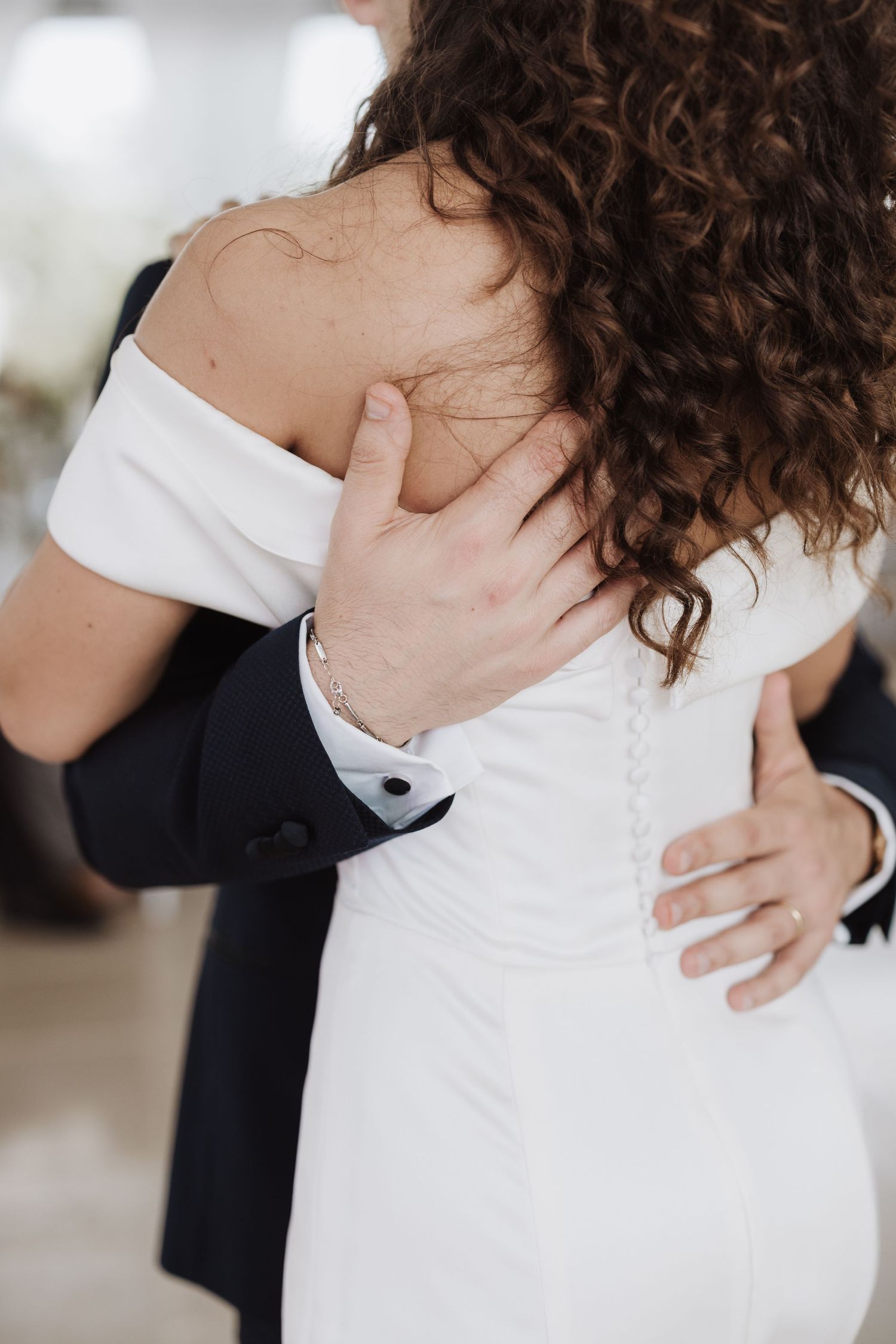 Close-up detail of an embrace showing the back of a white wedding dress.