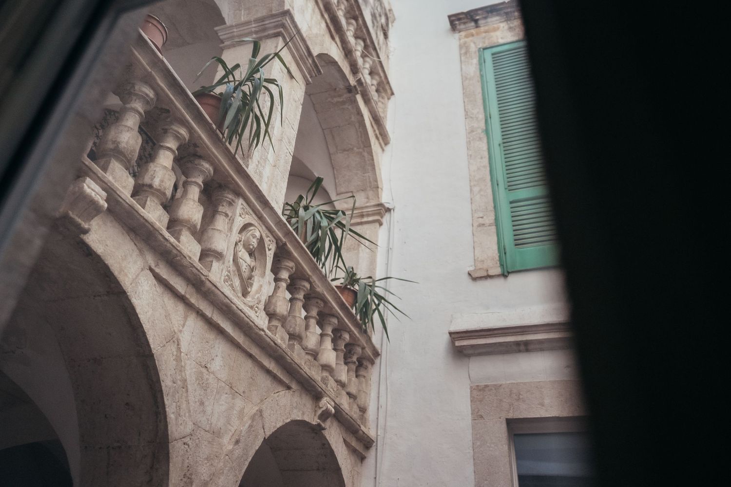 Mediterranean architectural detail showing arches and green shutters with plants.