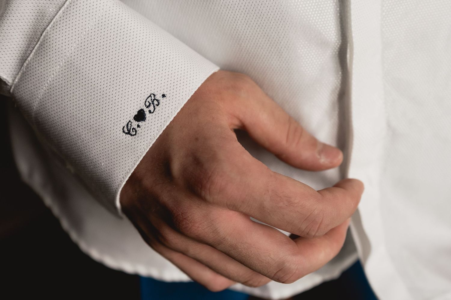 Close up detail of a white dress shirt sleeve with embroidered text.