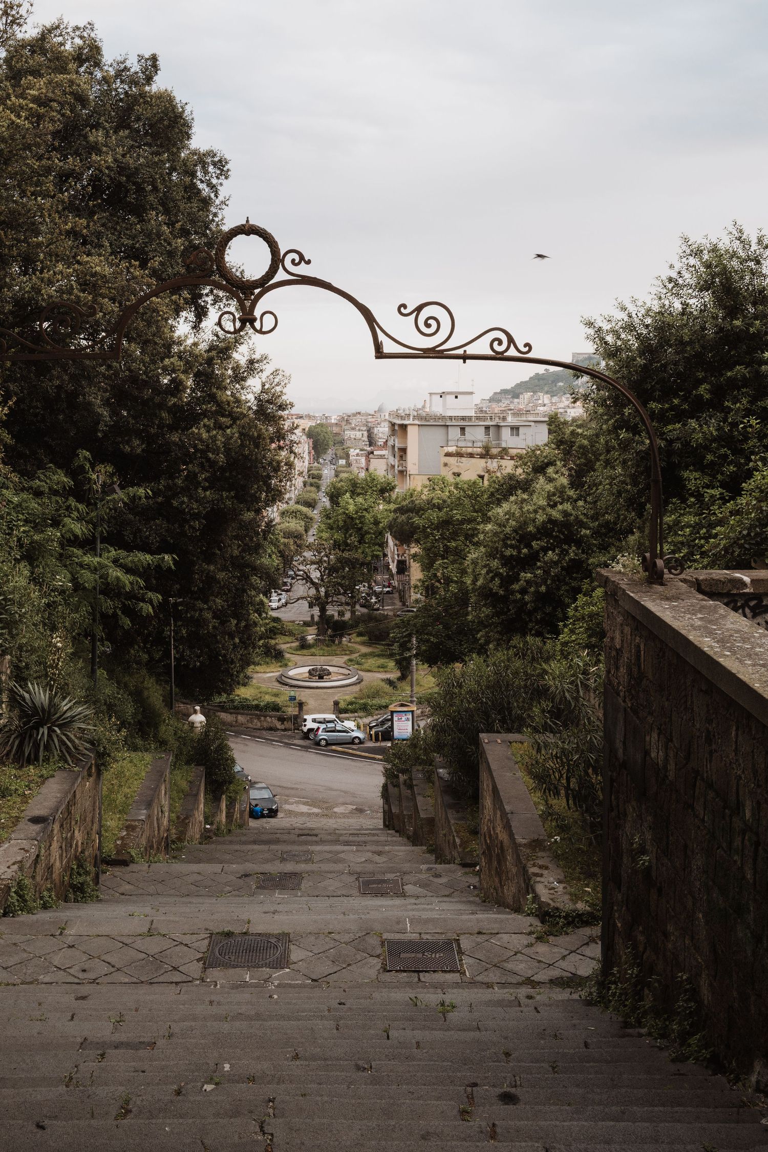 Decorative iron archway spans over steep stone steps descending into an urban neighborhood.