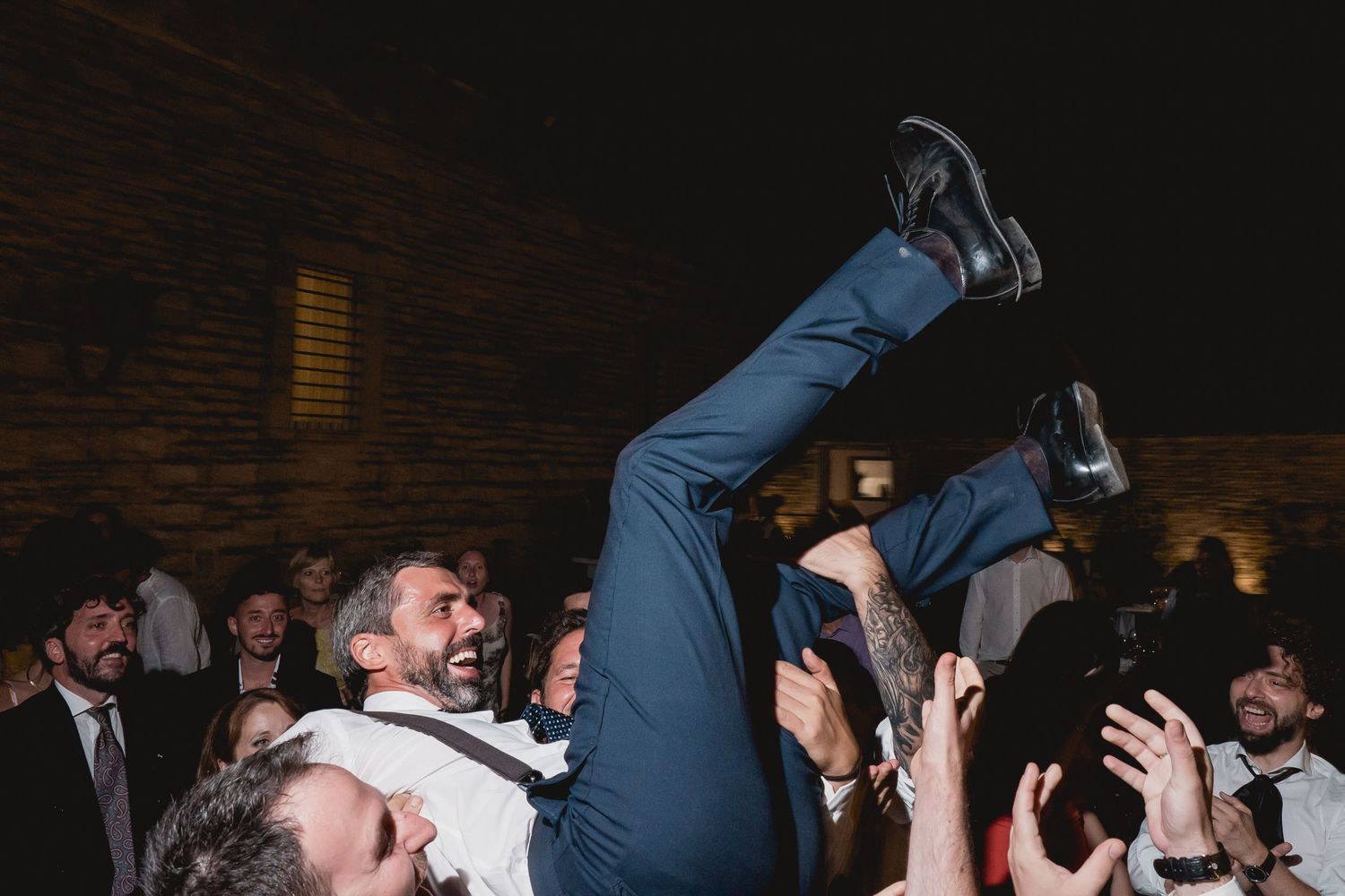 Wedding guests lift someone up during an energetic dance party celebration.