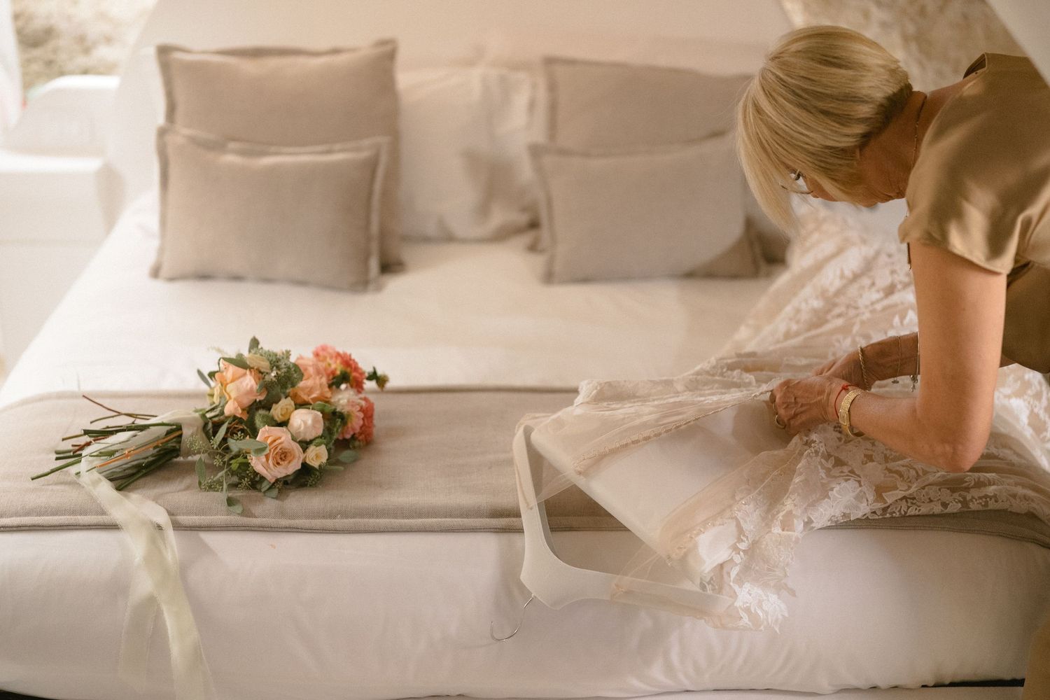 Delicate bridal bouquet lying on white bedding with someone adjusting details.
