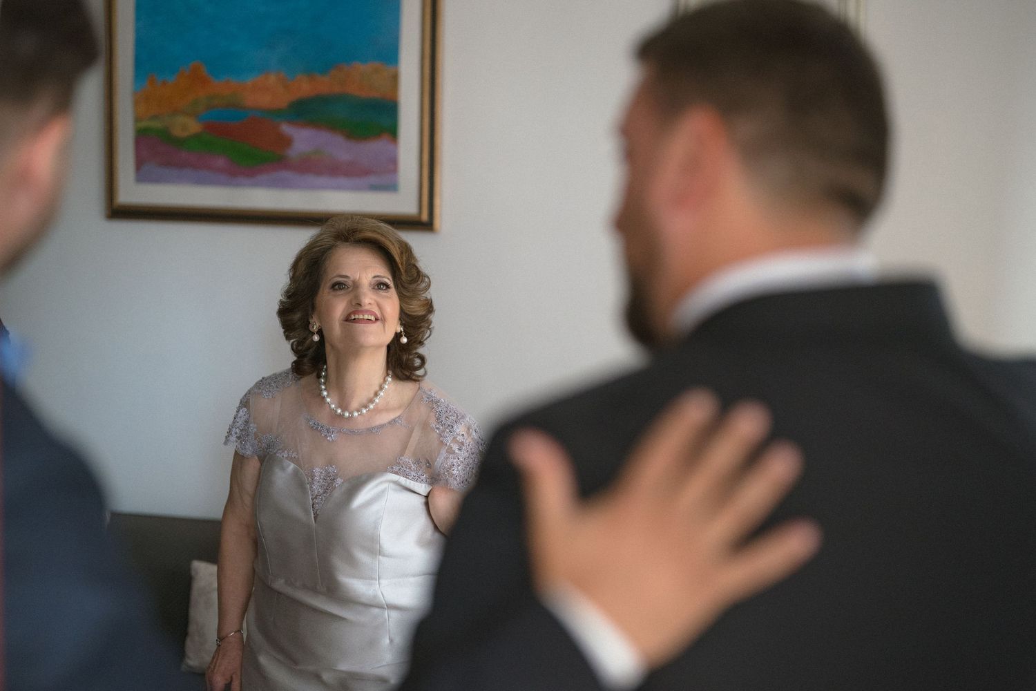 A candid wedding moment showing an emotional first look between loved ones in a room with colorful artwork on the wall.