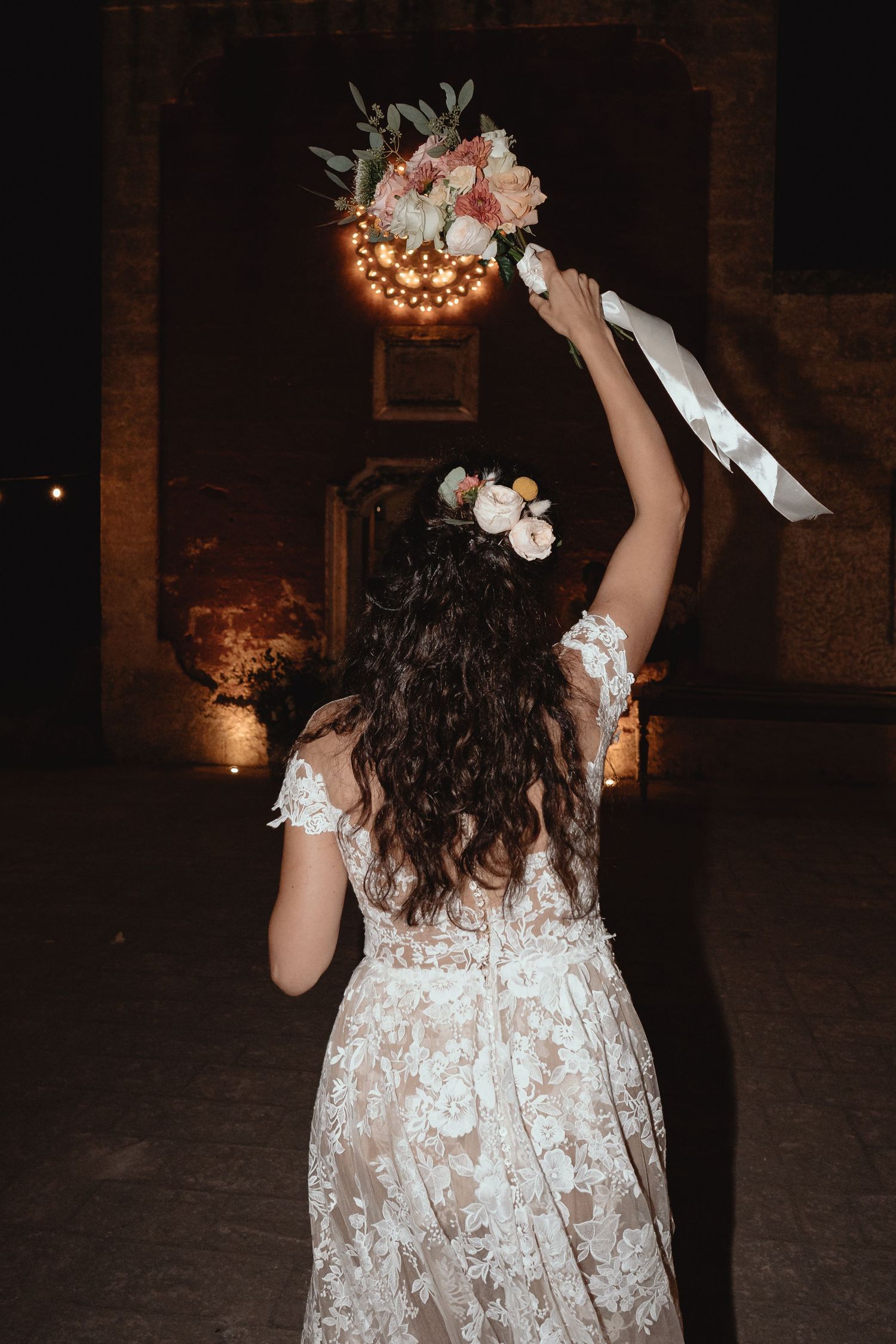 A white lace wedding dress silhouette against a dark background with string lights.